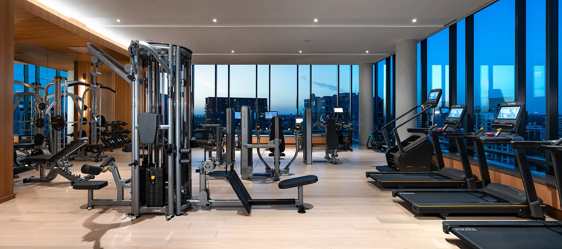 Luxurious high-rise gym with state-of-the-art fitness equipment, offering panoramic city views through floor-to-ceiling windows.