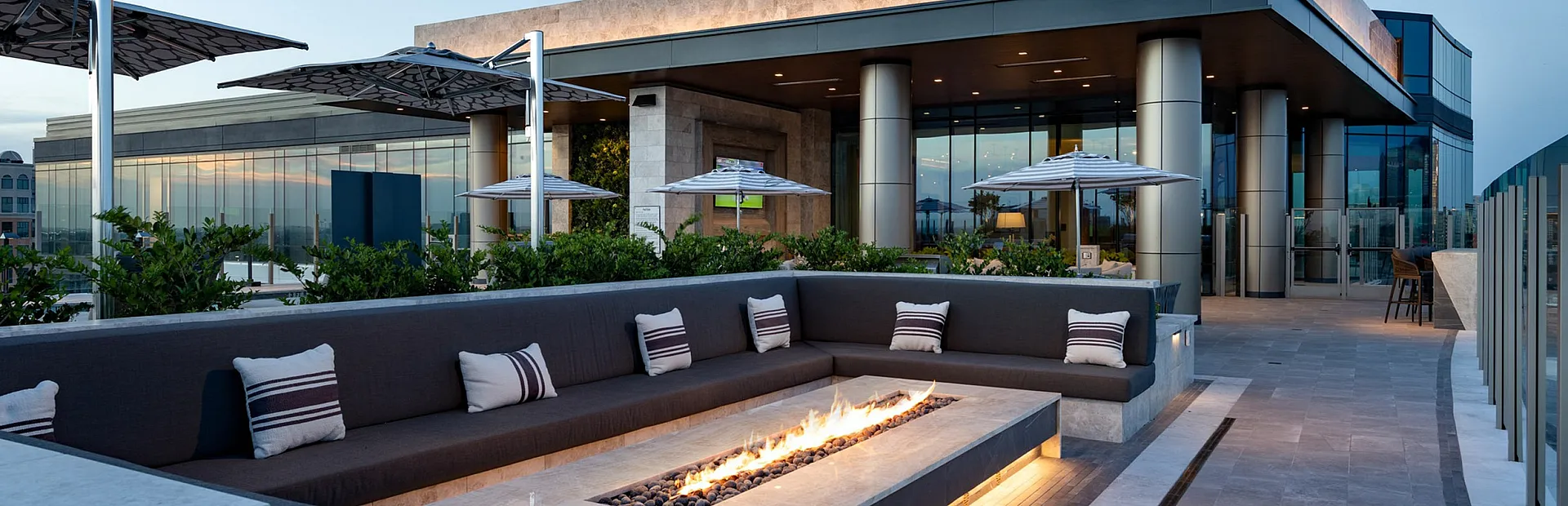 Luxurious rooftop terrace with modern fire pit, elegant seating, and panoramic city views at twilight.