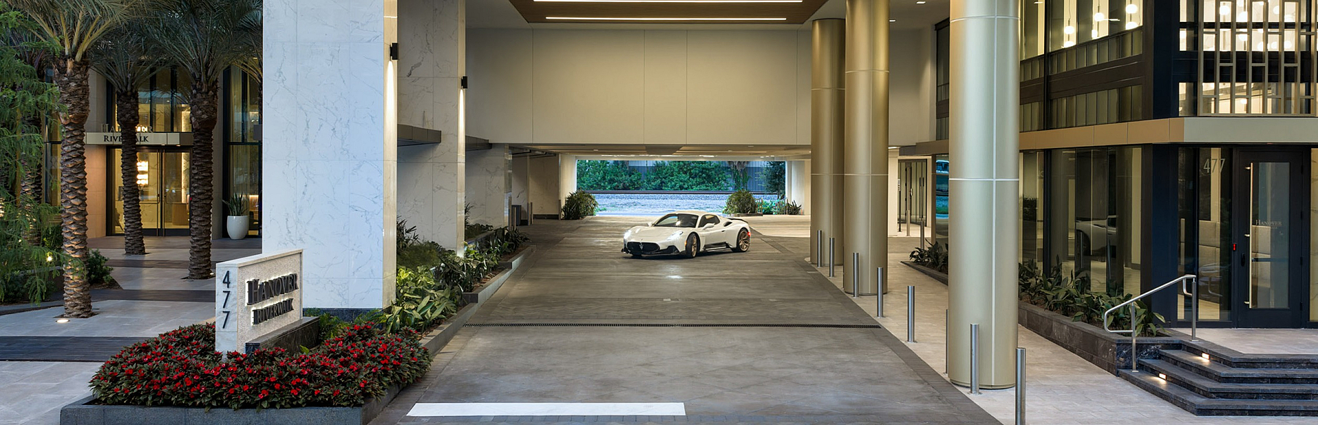 Elegant entrance of a modern apartment building with sophisticated lighting and lush greenery, showcasing luxury living.