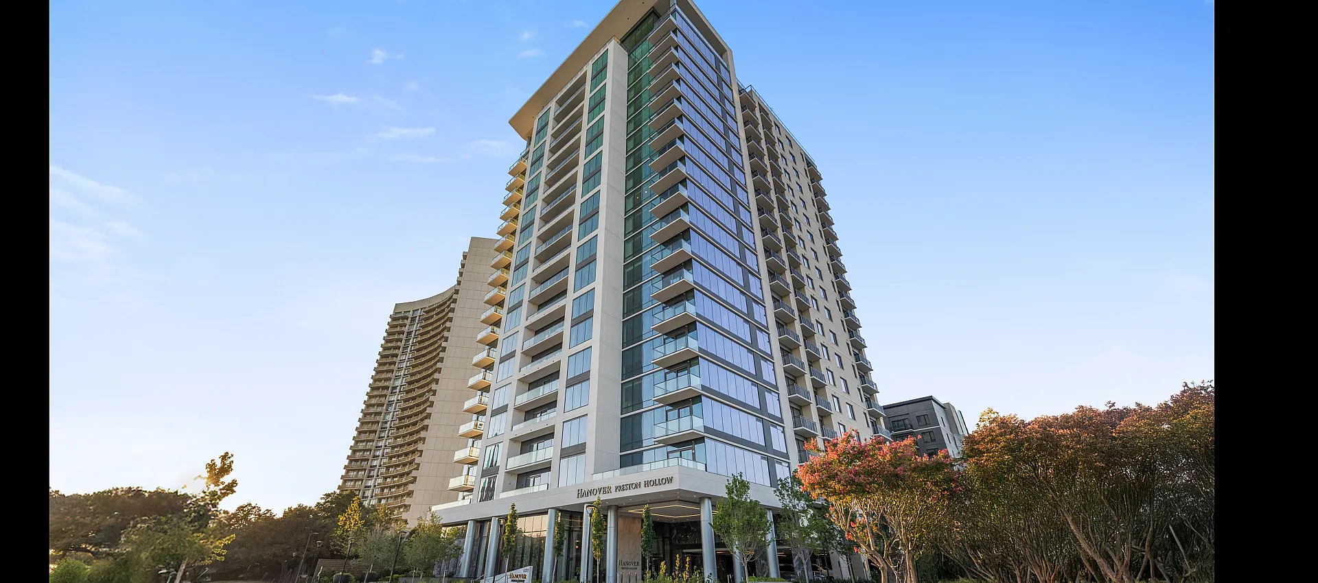 Elegant high-rise building with modern architecture and lush landscaping, under a clear blue sky.