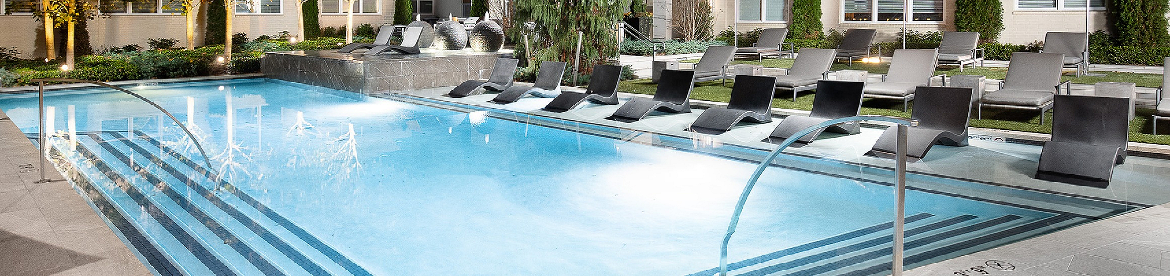 Elegant apartment complex with a sparkling outdoor pool, surrounded by modern architecture and ambient night lighting.