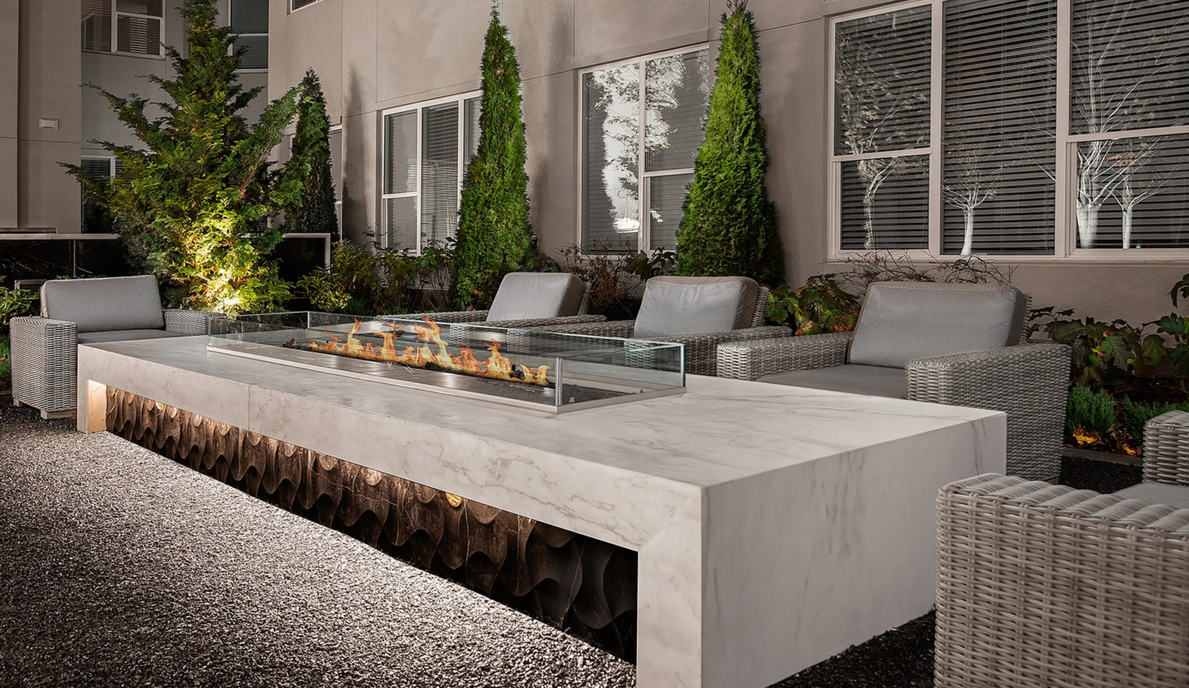 Chic outdoor lounge area with elegant fire pit, cozy wicker seating, and lush greenery backdrop.