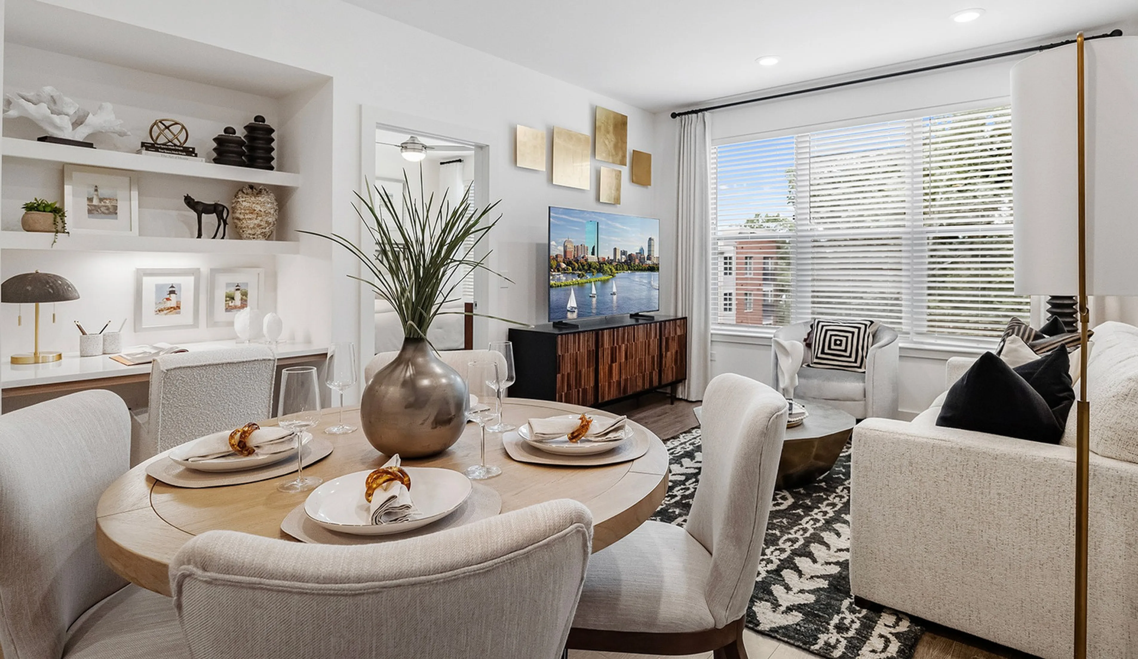 Contemporary living room and dining area with elegant decor, featuring a cozy white sofa, stylish wooden dining table set for three, and large windows with natural light.