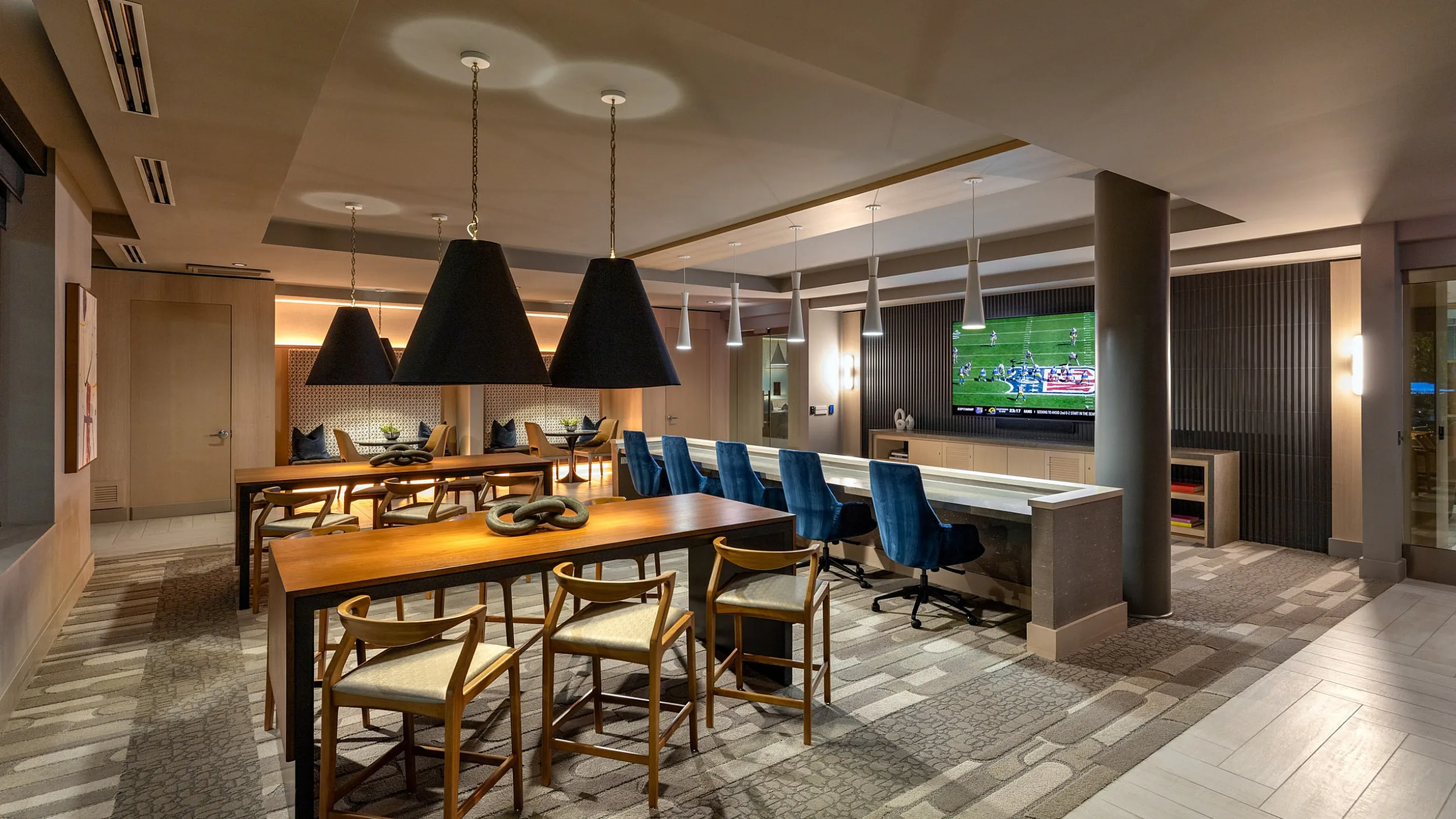 Elegant entertainment space featuring modern furniture, warm lighting, a long dining table, and a wall-mounted TV.