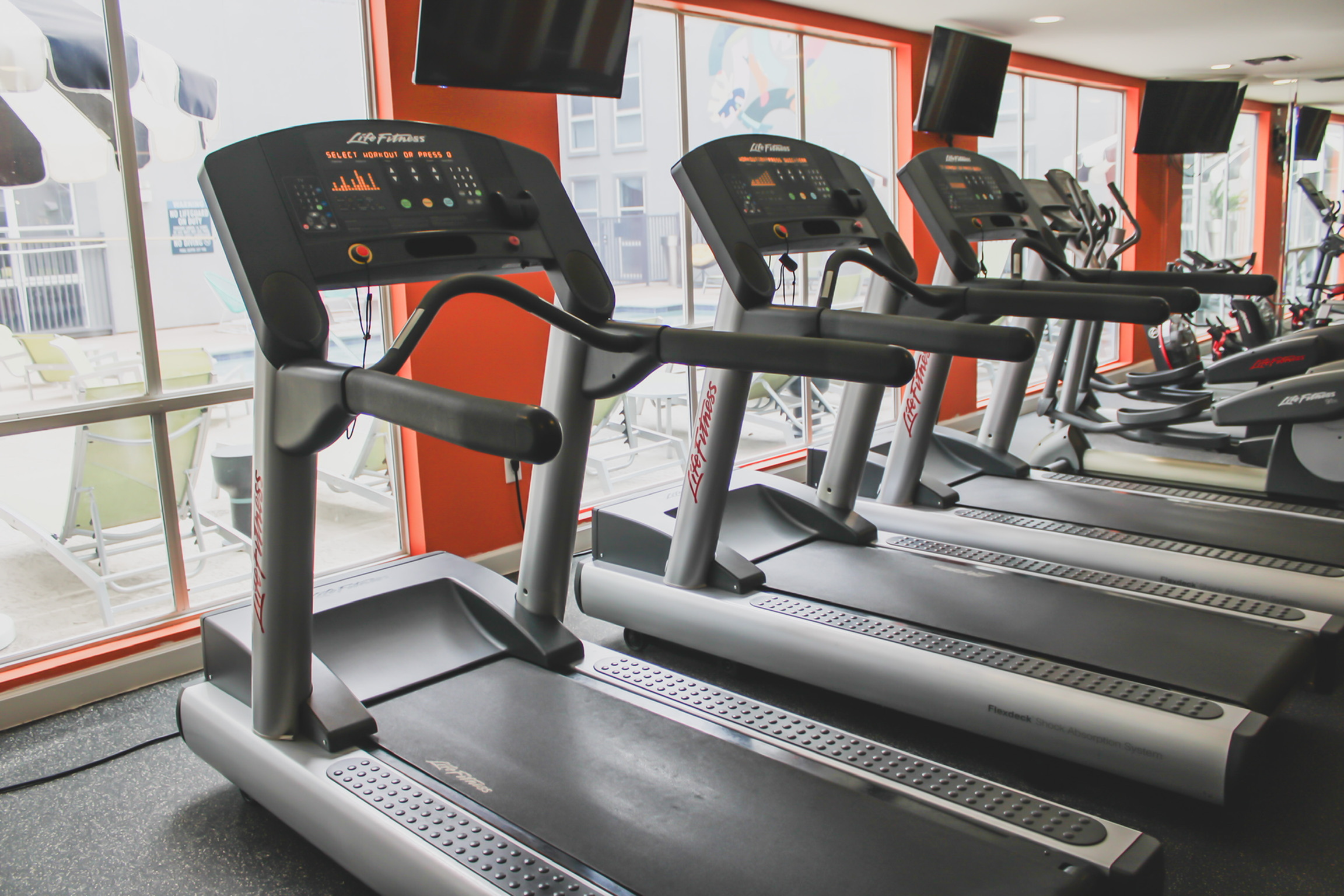 Apartments near University of Texas Austin with Modern fitness center showcasing state-of-the-art treadmills with bright, inviting windows overlooking an outdoor pool area.