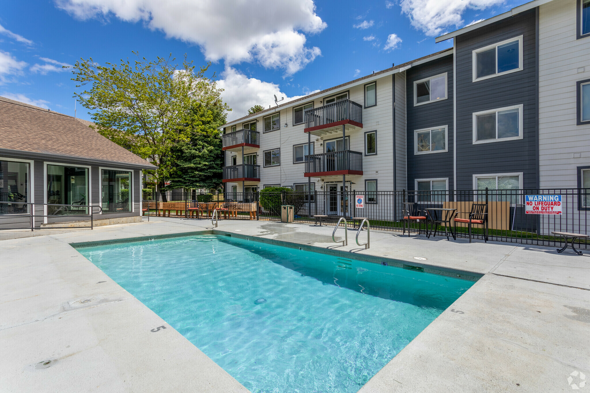 Inviting outdoor pool area with modern apartment building and lush greenery under a bright blue sky.