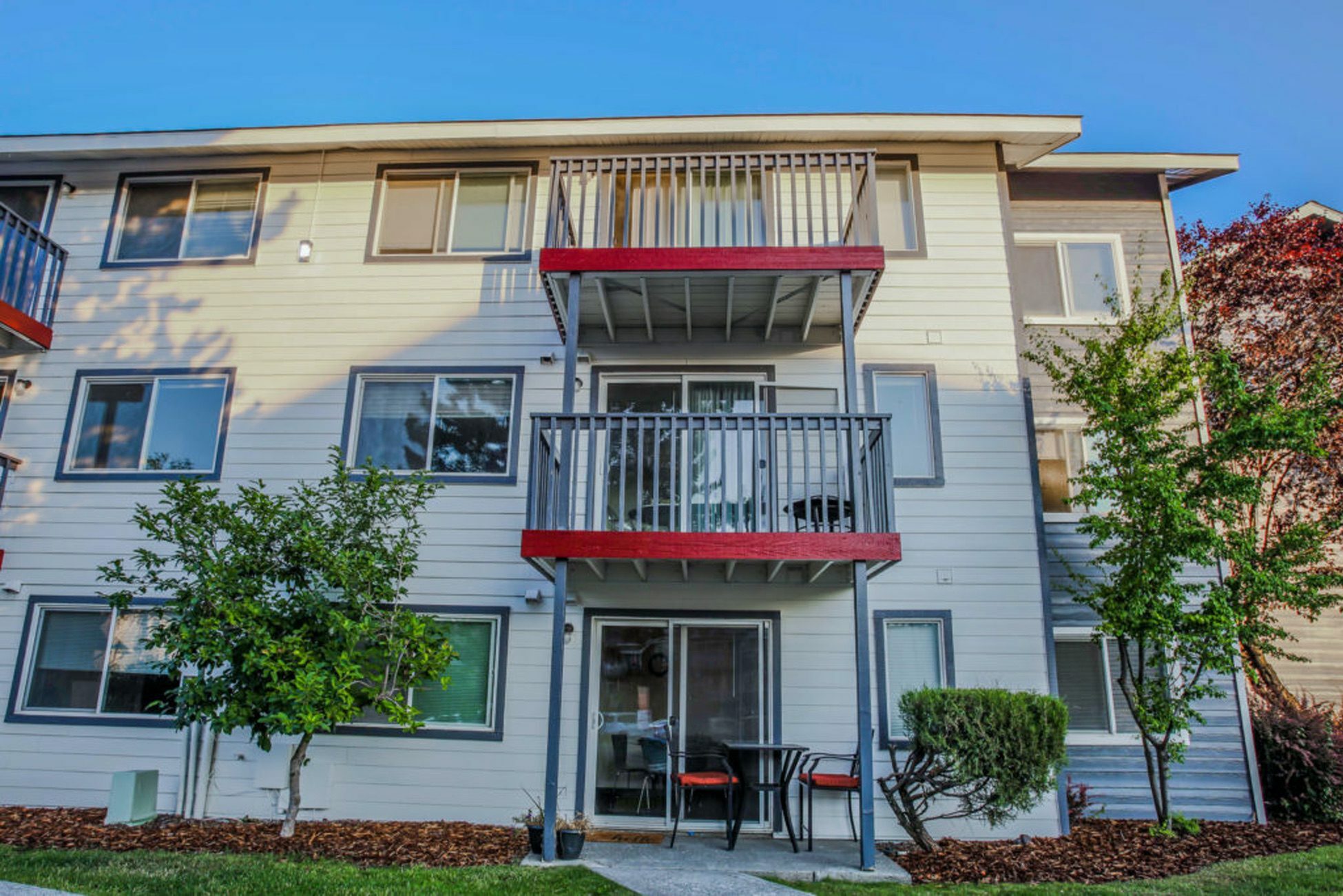 Bright and welcoming three-story apartment building with balconies and lush greenery.