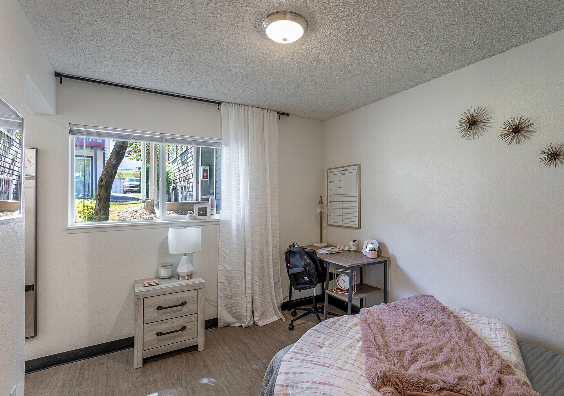 Stylishly furnished bedroom with a desk, modern lamp, and window view, featuring neutral tones and decorative accents.