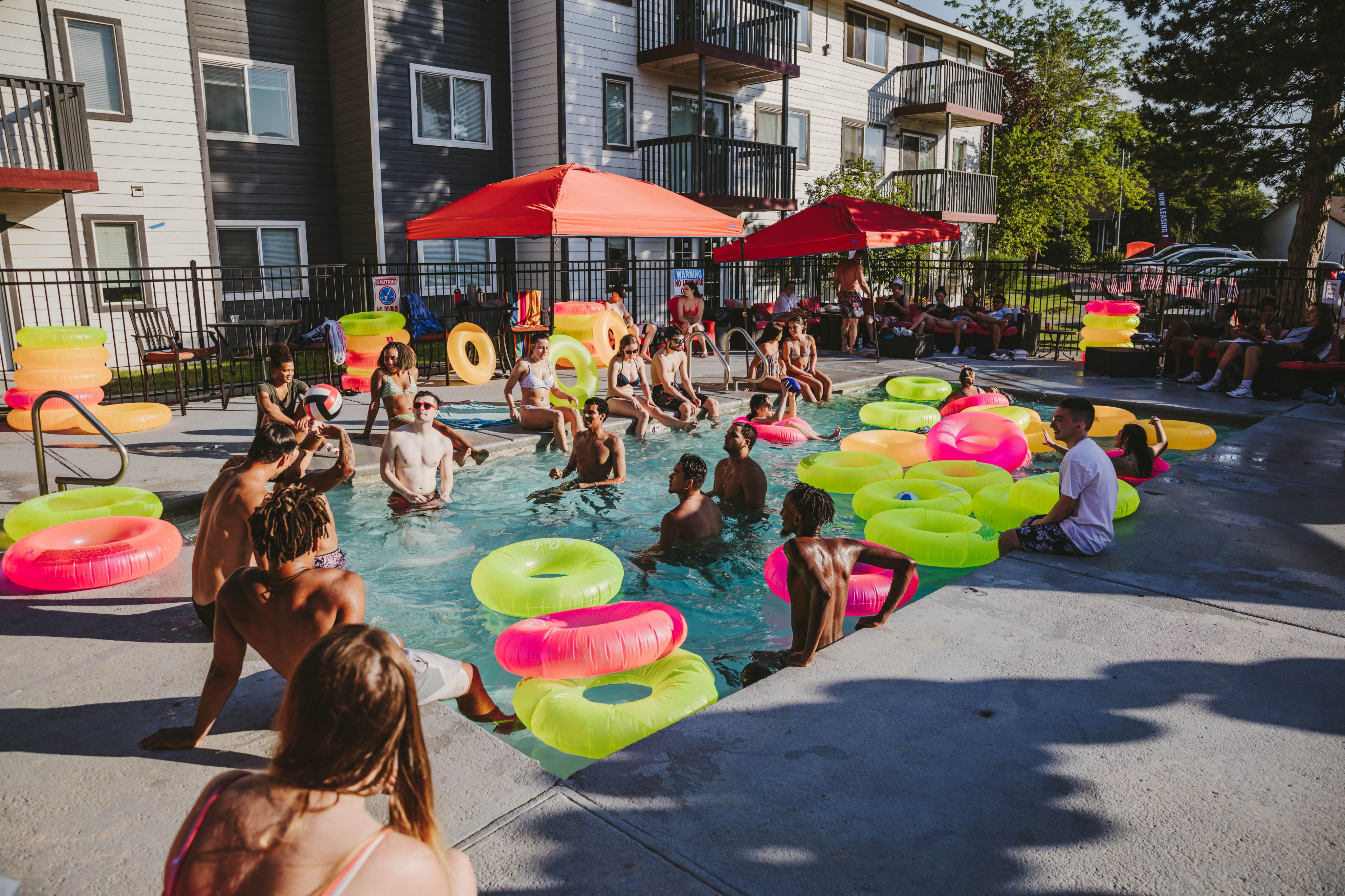 Lively pool area with people enjoying the sun and using colorful float rings.