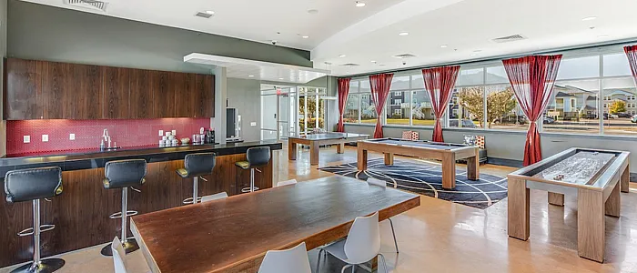 Spacious recreational area with modern bar seating, sleek wooden tables, and bright natural lighting; perfect for social gatherings.