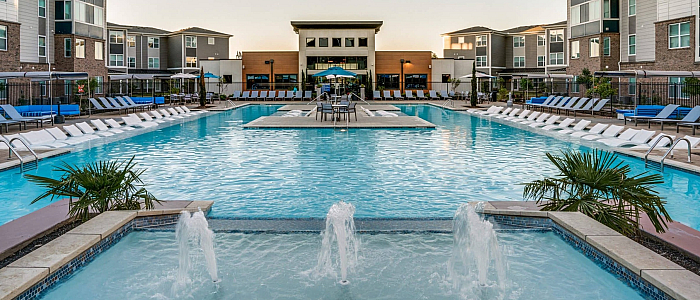 Luxurious apartment complex with a sparkling resort-style pool, surrounded by modern buildings and stylish lounge chairs.