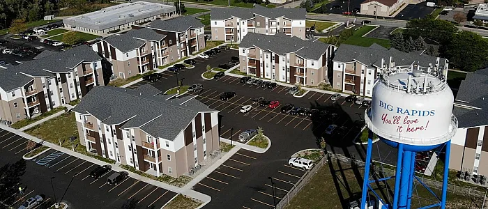 Scenic aerial view of modern apartment complex in a lush, green neighborhood with ample parking and nearby amenities, highlighted by a vibrant Big Rapids water tower.
