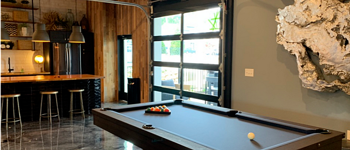 Chic lounge area with a sleek pool table, rustic wooden accents, and an open kitchen with modern bar seating, ideal for entertaining.