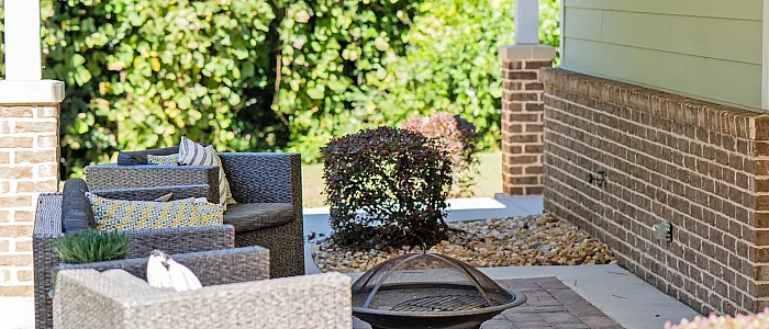 Charming outdoor seating area with cozy wicker furniture, brick accent wall, and lush greenery, perfect for relaxation.
