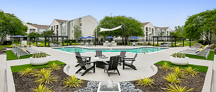 Inviting apartment complex exterior featuring a sparkling swimming pool surrounded by lush landscaping and stylish outdoor seating, perfect for relaxation.