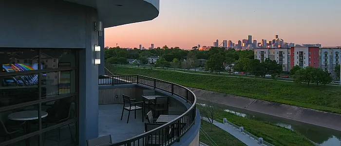 Modern balcony with sleek furniture offering breathtaking sunset views of the city skyline and lush green surroundings.