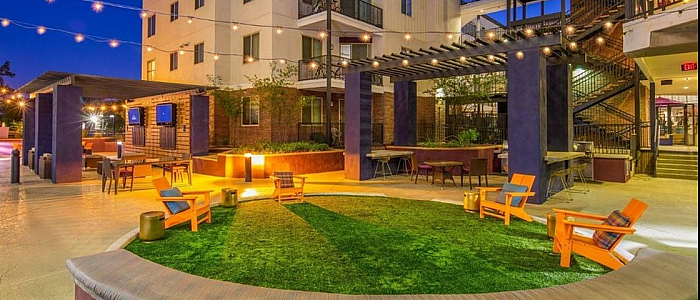 Vibrant urban courtyard with cozy seating, glowing string lights, and modern apartment buildings at dusk.