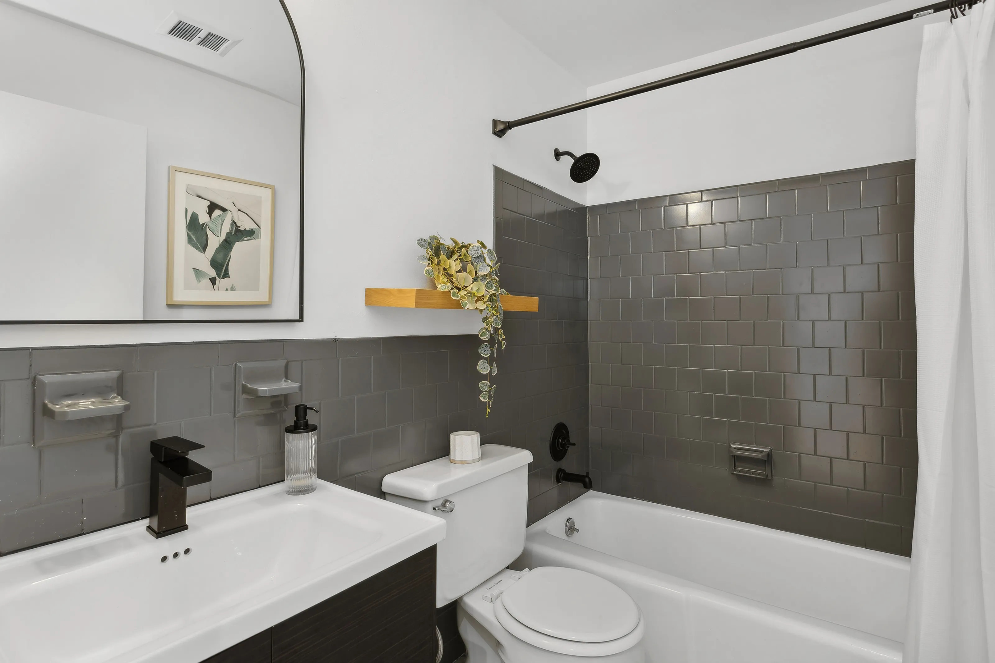 Renovated bathroom at ReNew Parkville with dark grey subway tile and dark grey backsplash, matte black finishes, and modern mirror.