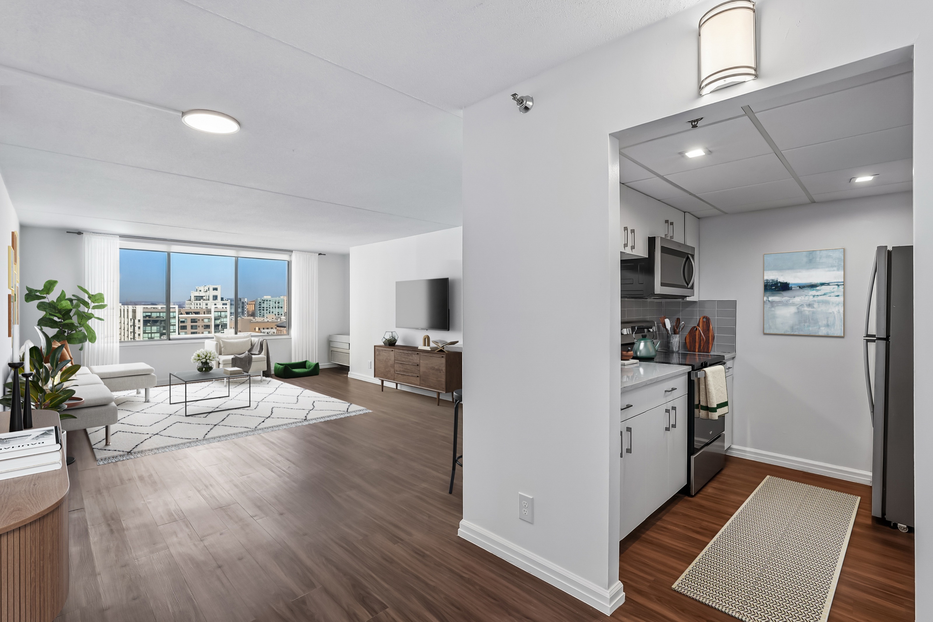 An open-concept kitchen and living room at ReNew Logan Square showcases white quartz countertops and stainless steel appliances in the kitchen with modern furniture in the living room.