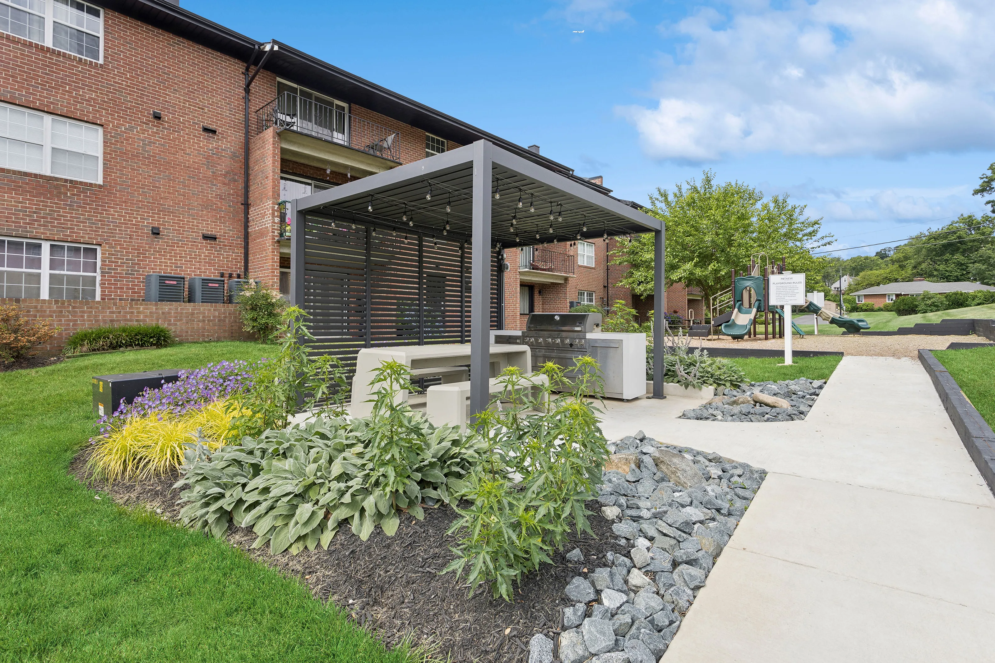 Gas grill and pergola at ReNew Parkville surrounded by lush landscaping.
