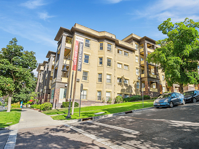 Elegant apartment complex on a sunny, tree-lined street, showcasing modern architecture and vibrant greenery.