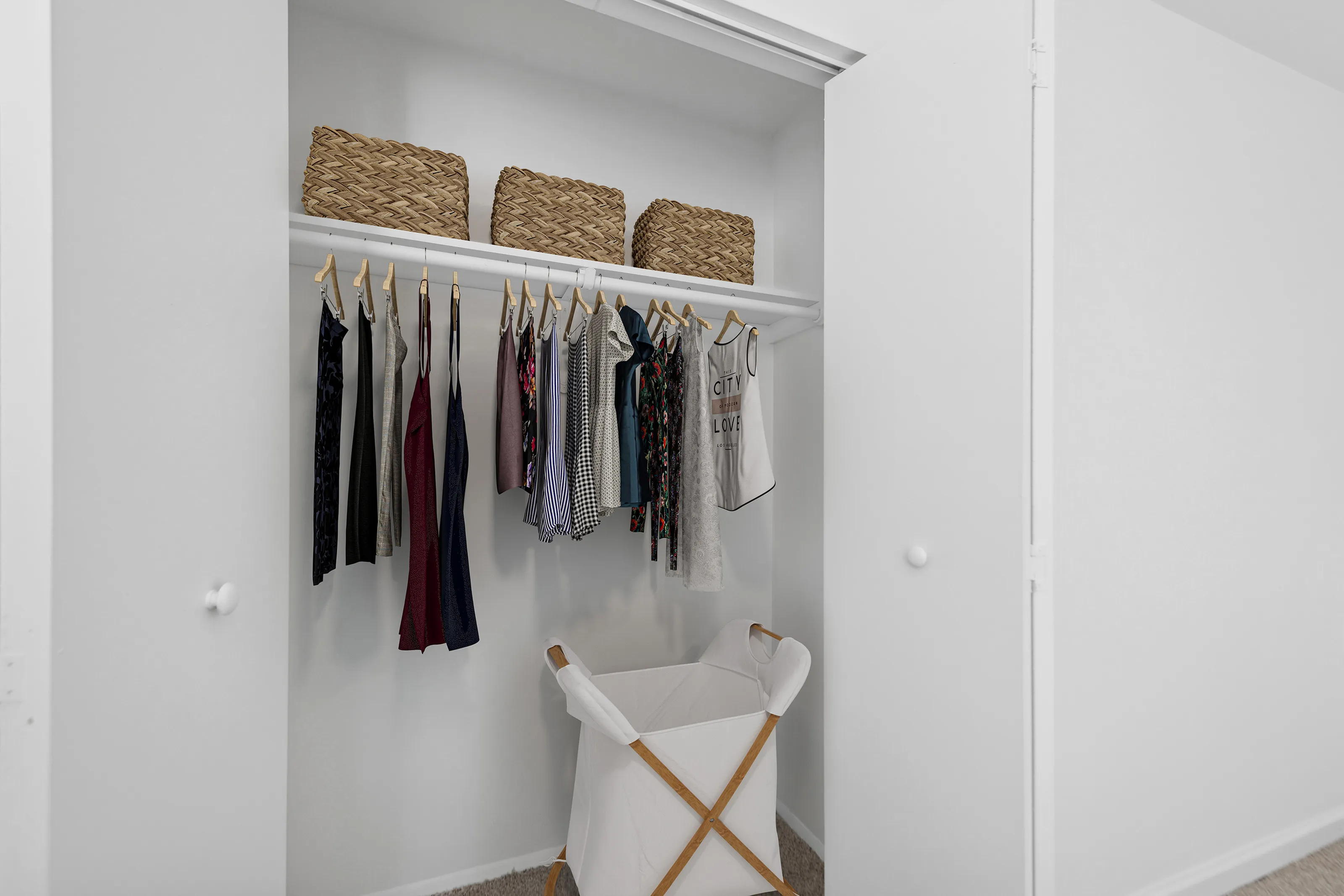 Chic white closet with wooden hangers, organized clothing, and woven baskets.