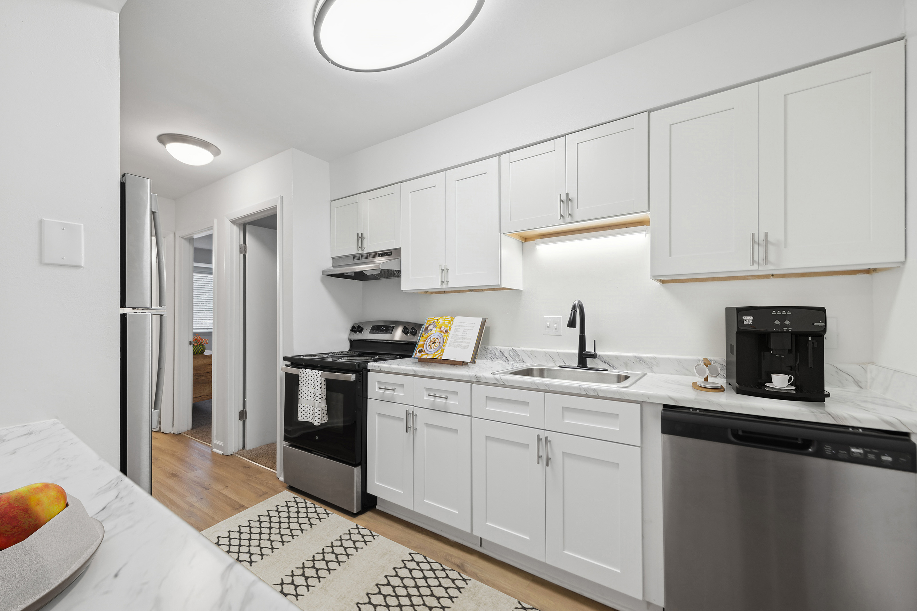 Contemporary kitchen with stainless steel appliances, white cabinetry, and marble countertops.