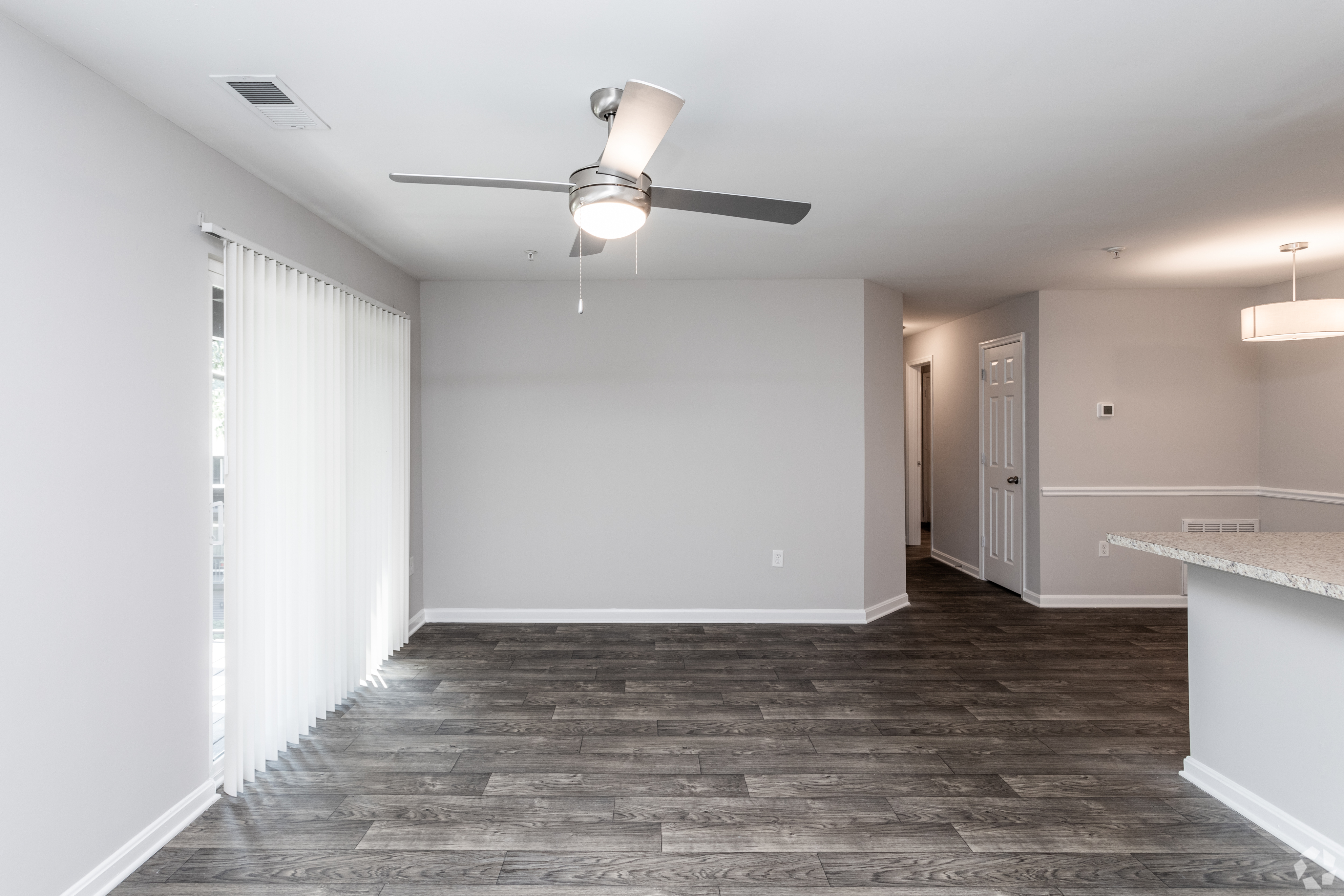 Spacious living room with sleek ceiling fan, wood-style flooring, and light-filled atmosphere.