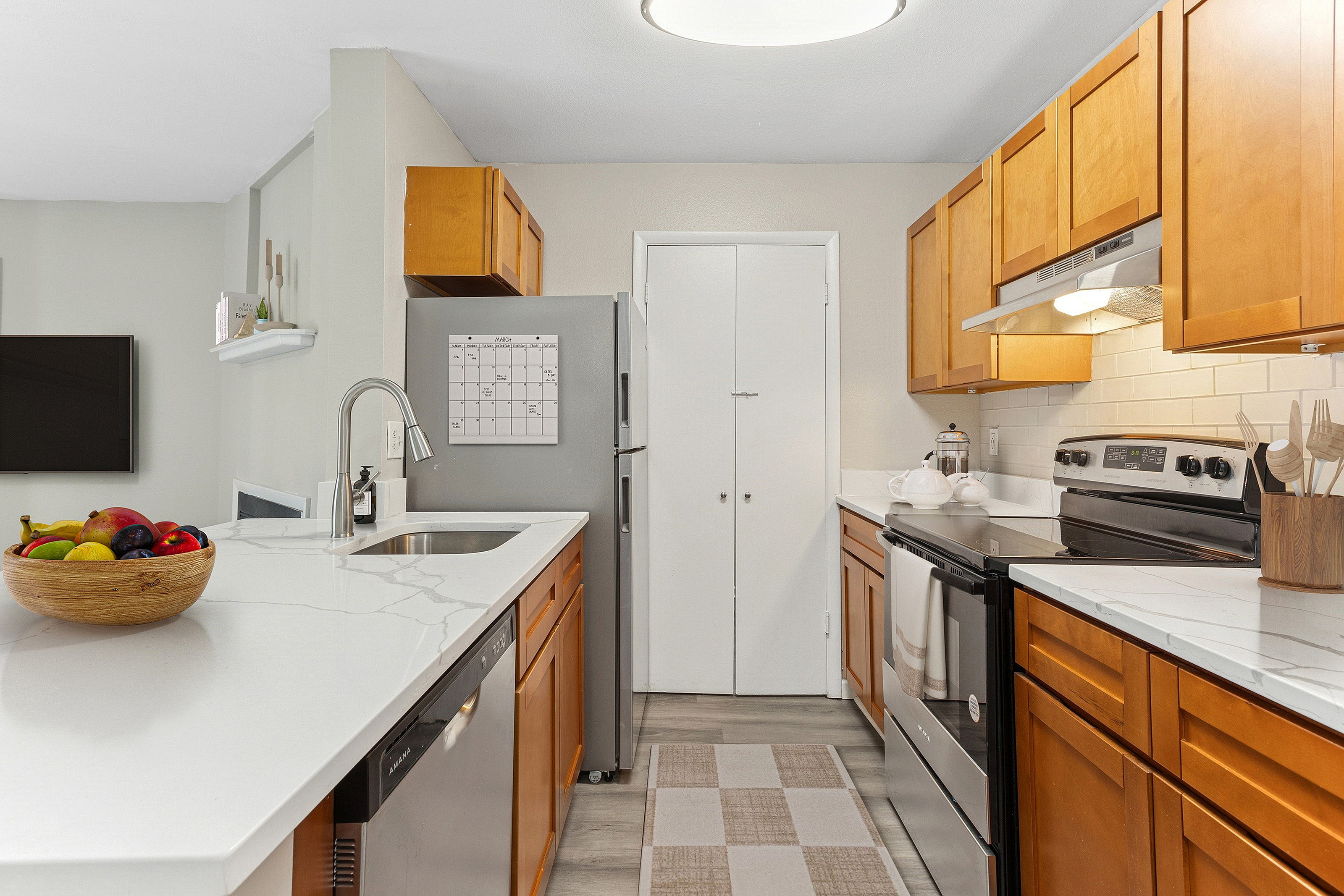 Modern kitchen with sleek white countertops, stainless steel appliances, and warm wooden cabinetry, offering a stylish and functional cooking space.