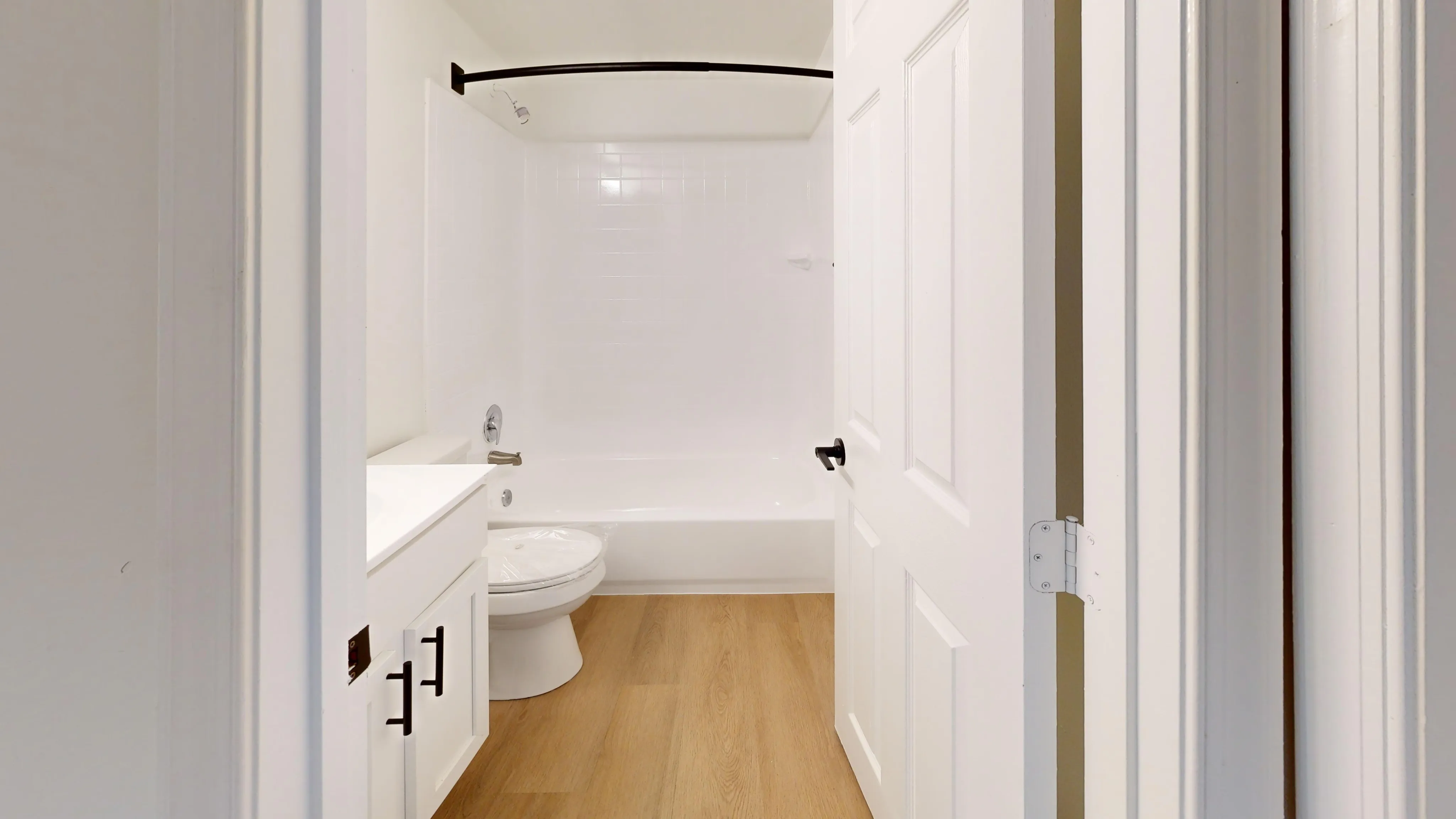 Elegant bathroom with modern white fixtures, a clean bathtub, and warm wood flooring creating a serene atmosphere.