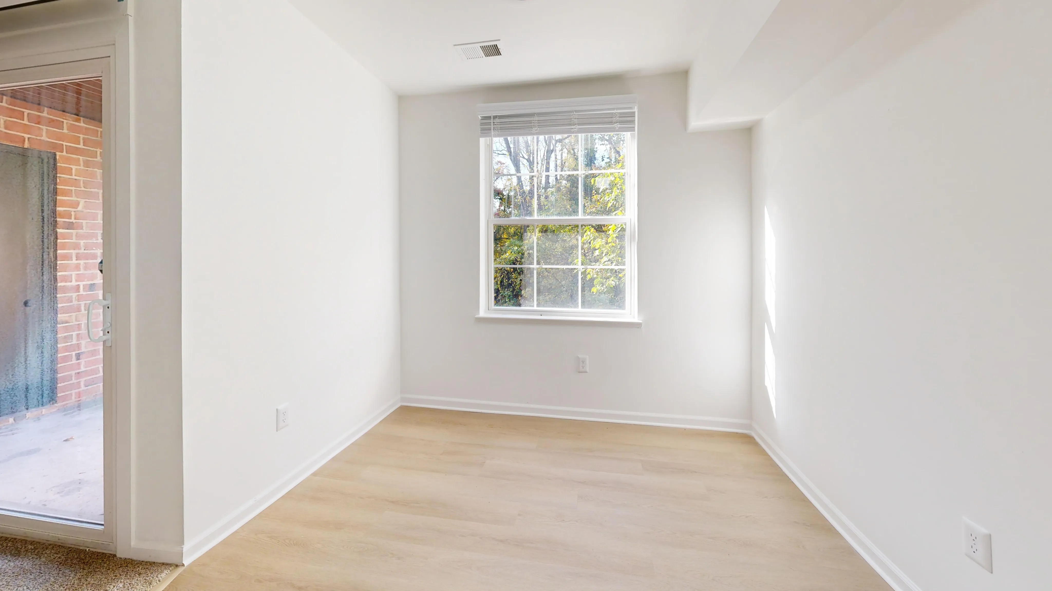 Bright, cozy room with light wood flooring, large window offering a scenic view, and adjacent sliding door leading to an outdoor area.