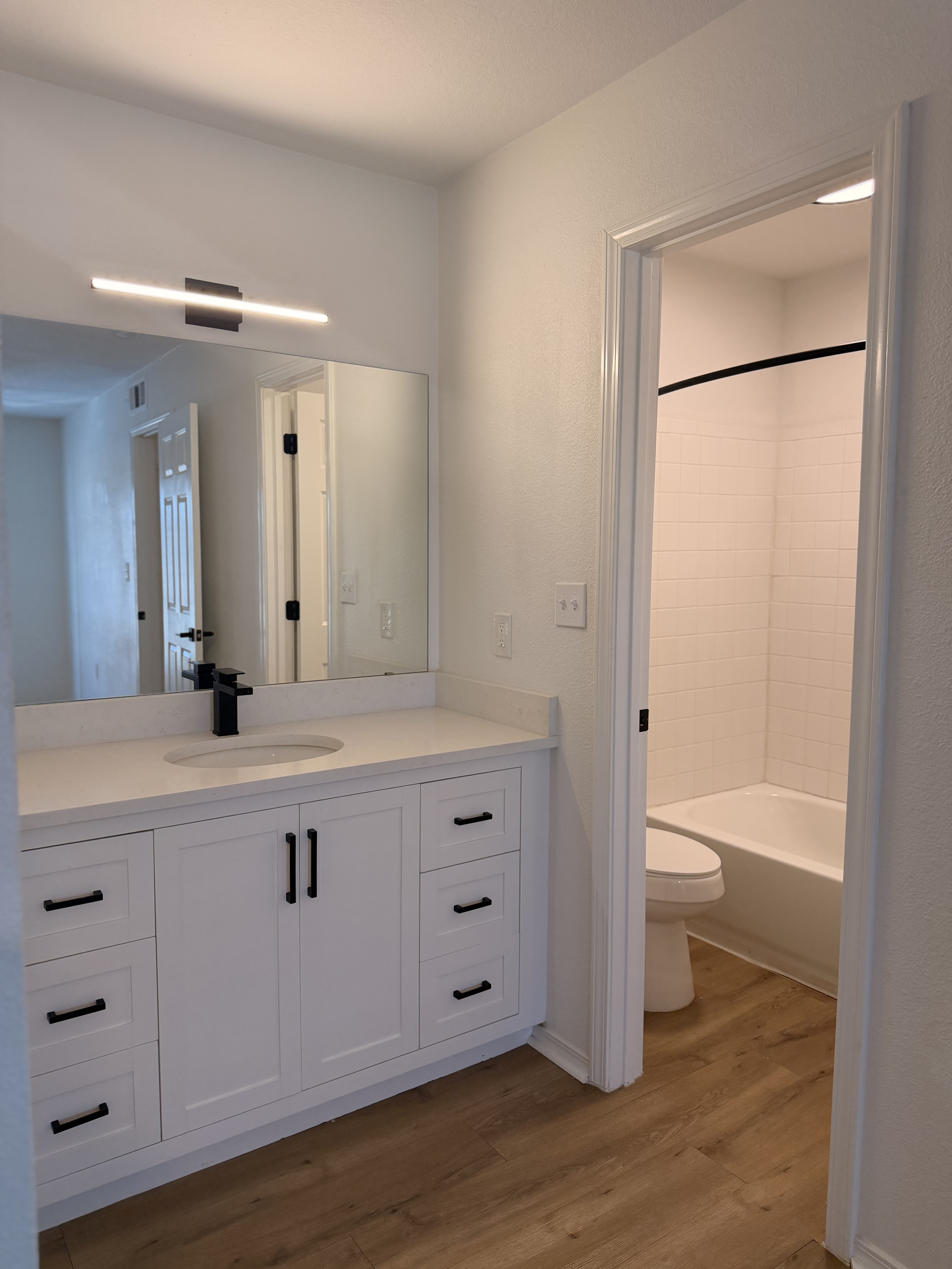 Elegant bathroom with modern white vanity, sleek black faucet, and bright lighting, adjacent to a cozy bathtub.