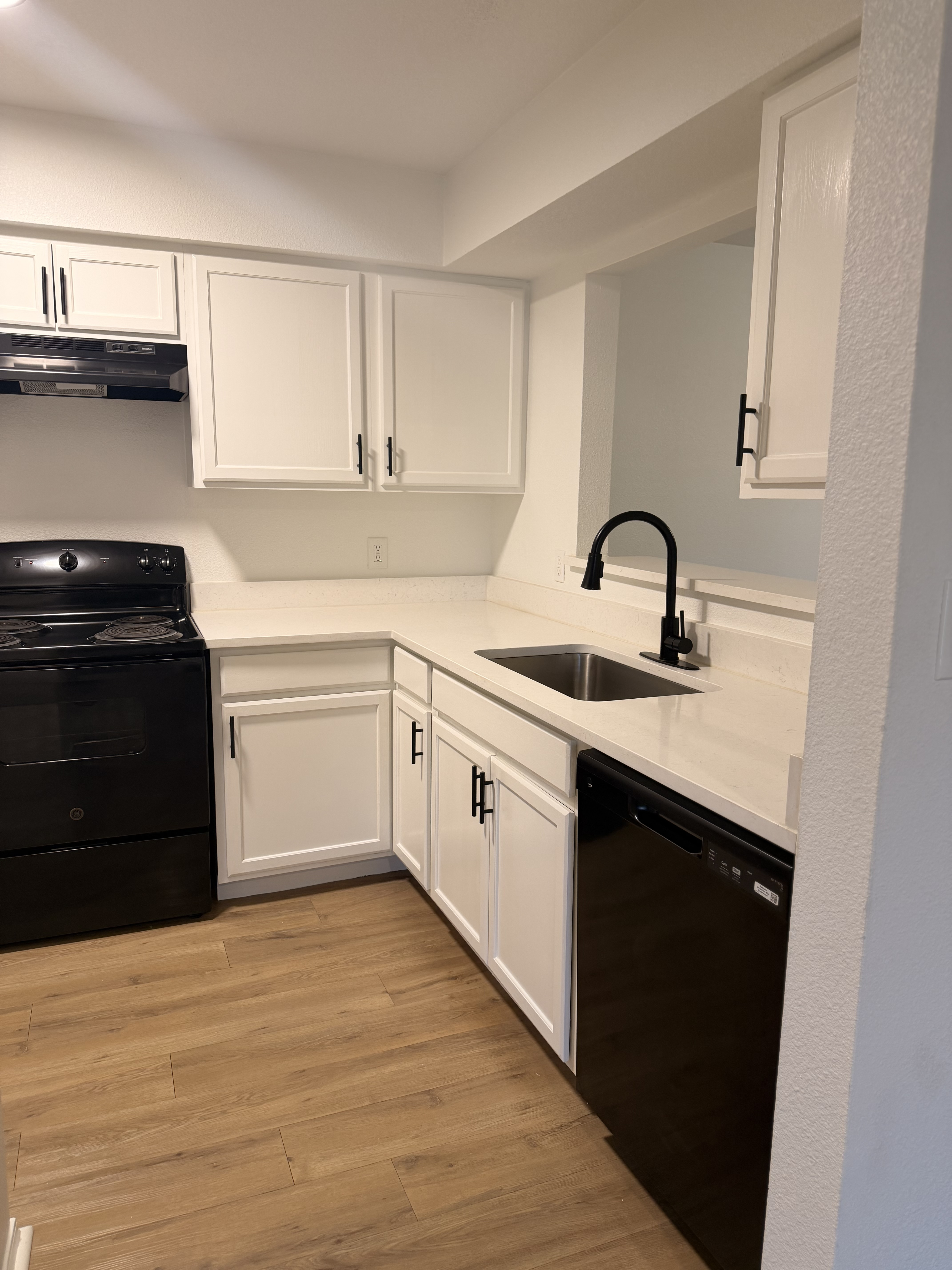 Modern kitchen featuring sleek black appliances, crisp white cabinetry, and elegant wood flooring.