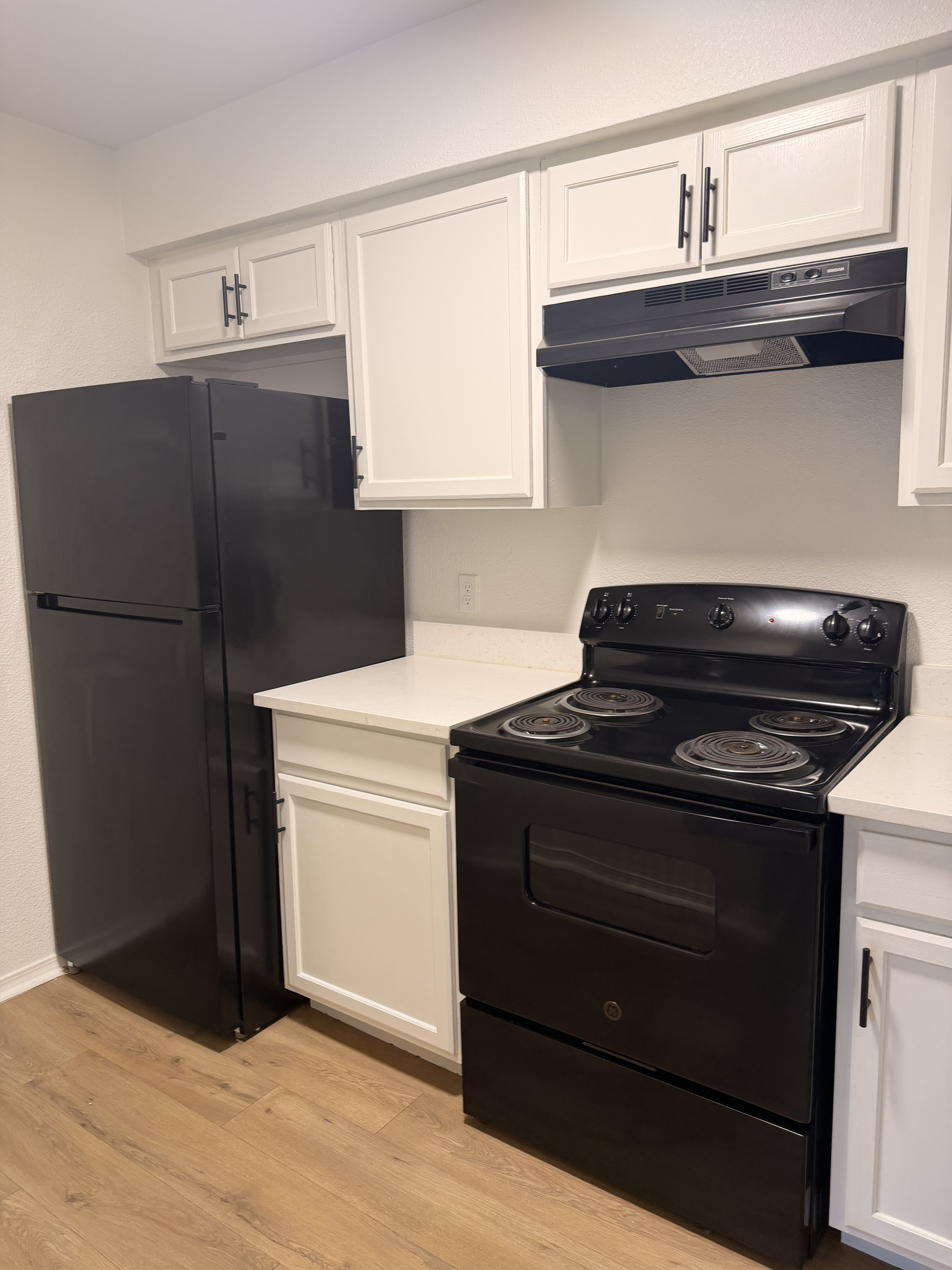 Modern kitchen with sleek black appliances, white cabinetry, and elegant wood flooring.