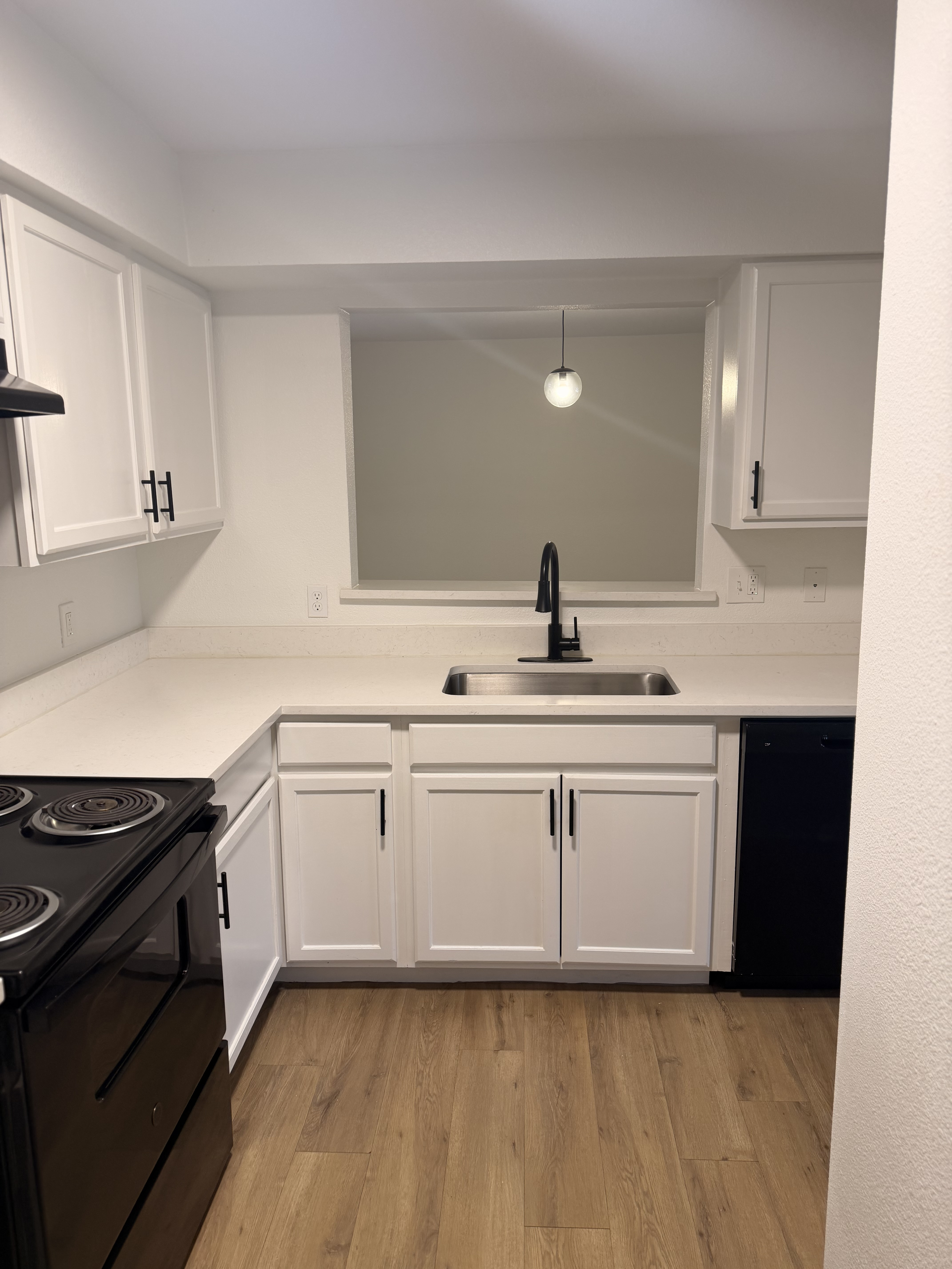Modern kitchen with sleek black appliances, stylish white cabinetry, open shelving, and warm wood flooring.