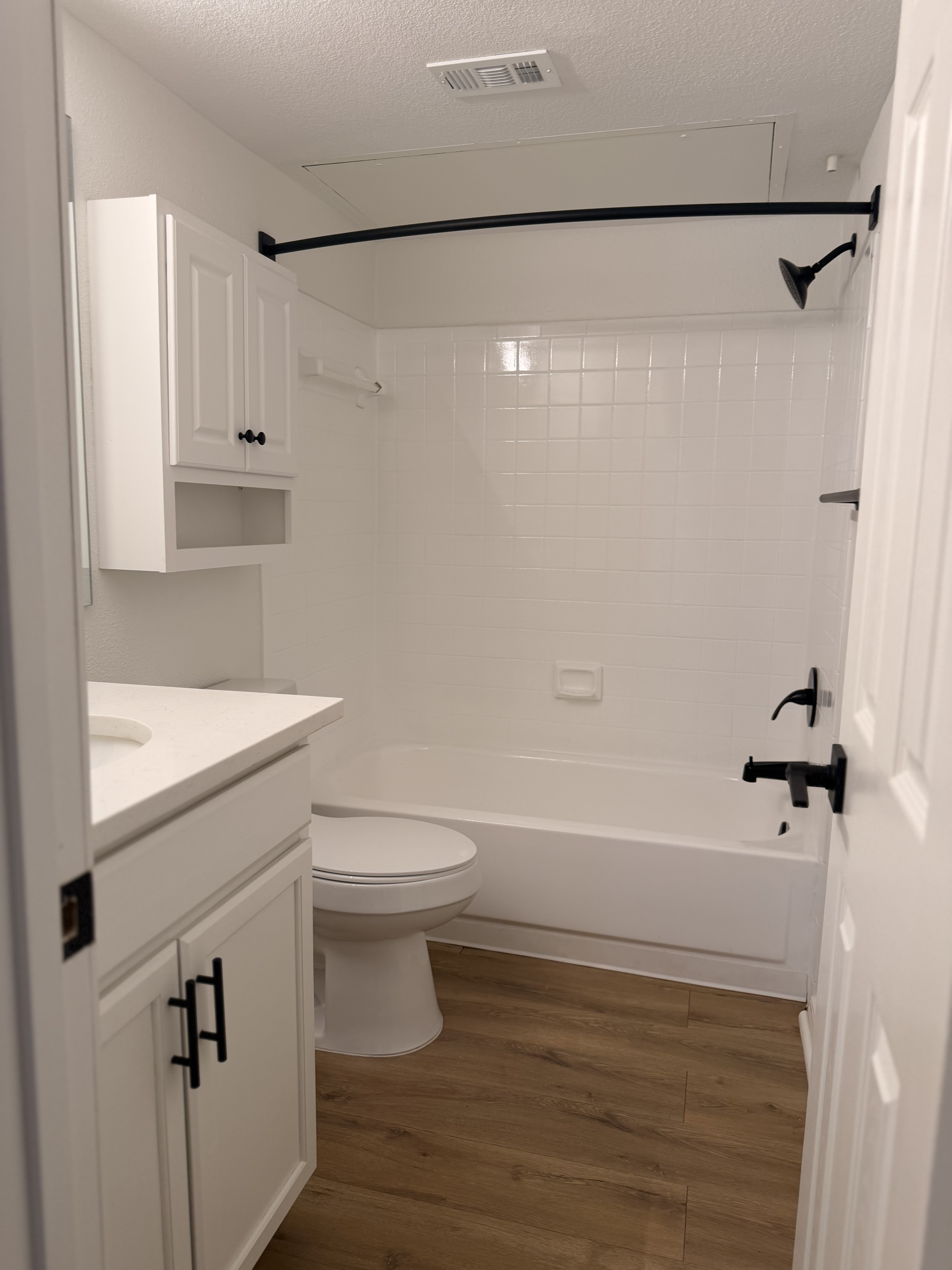 Elegant modern bathroom featuring sleek white cabinetry, a bathtub with contemporary fixtures, and stylish wood flooring.