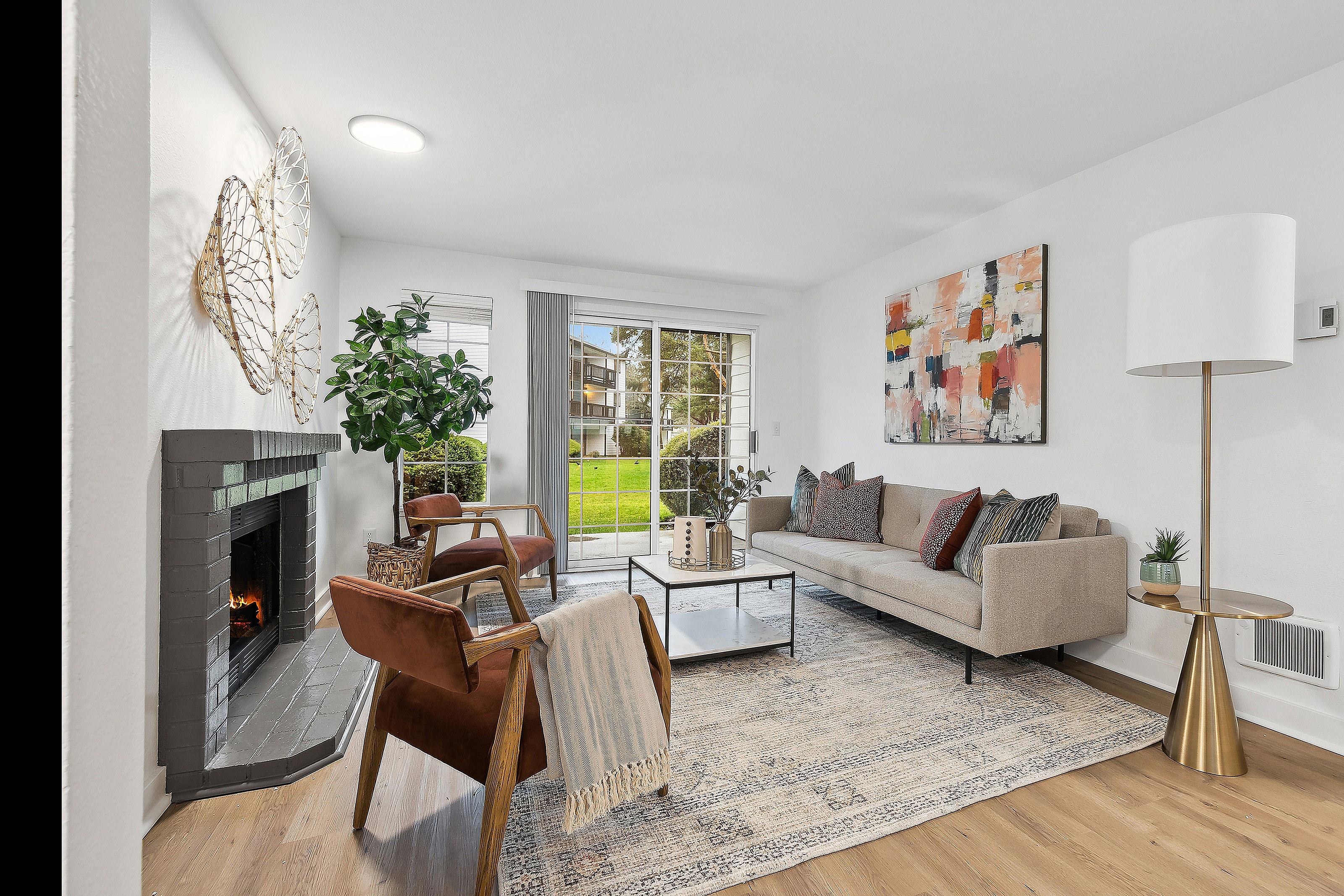 Inviting living room with elegant decor, cozy fireplace, modern furniture, and abundant natural light from large sliding glass doors overlooking lush greenery.