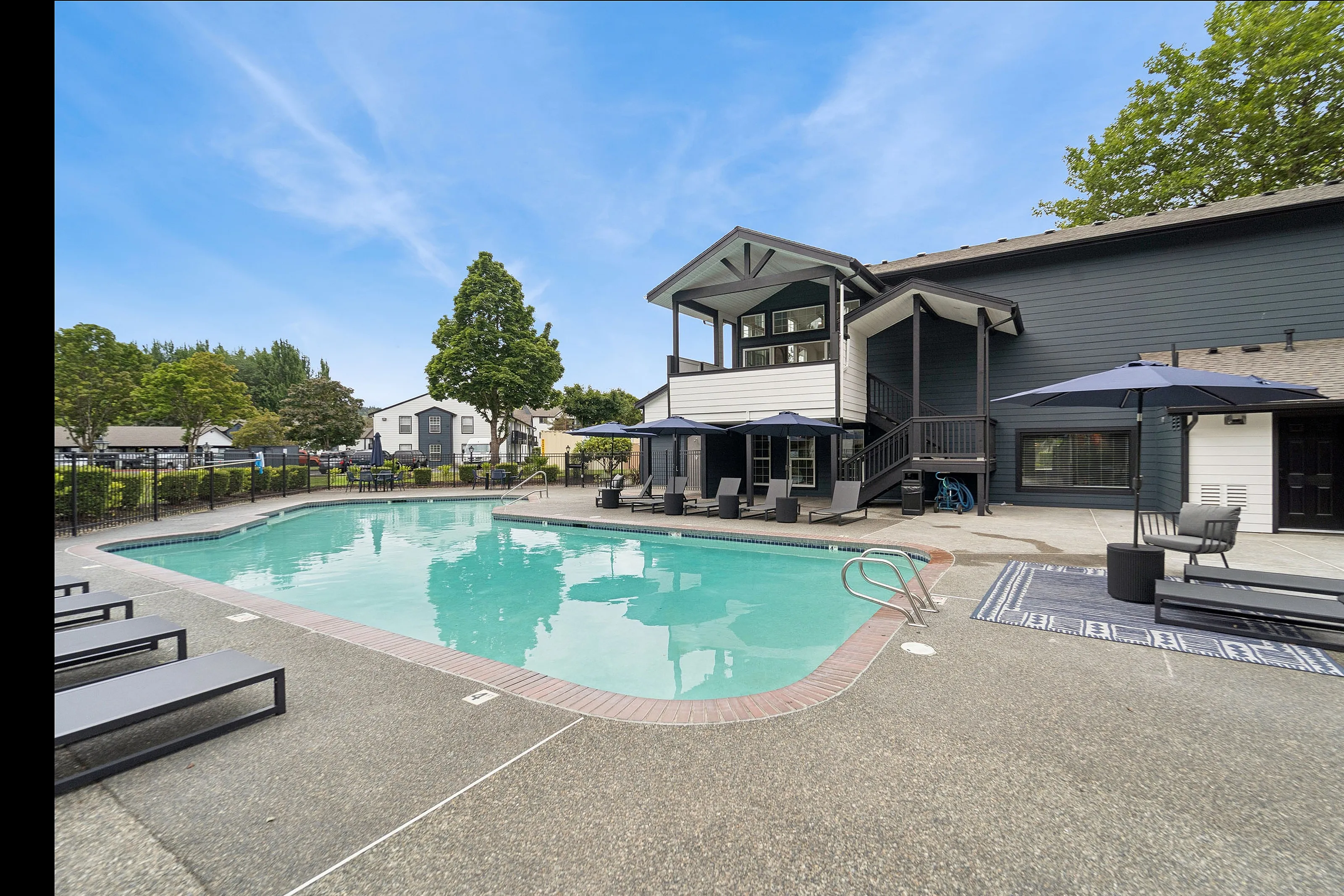 Exquisite apartment complex showcasing a pristine swimming pool, stylish lounge chairs, and vibrant landscaping under a clear blue sky.