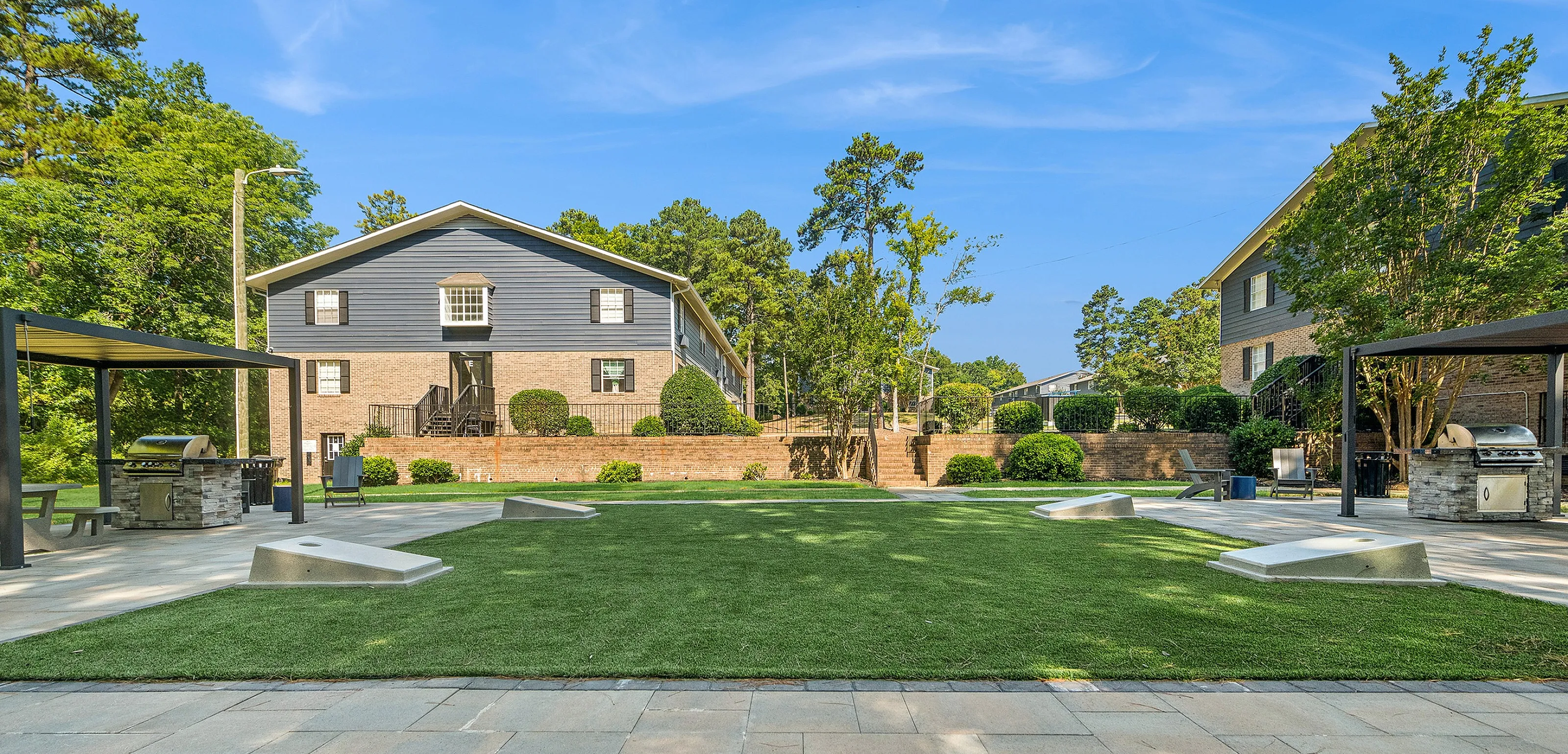 Inviting outdoor area with well-maintained lawns, shaded seating, and modern grill stations adjacent to residential buildings.