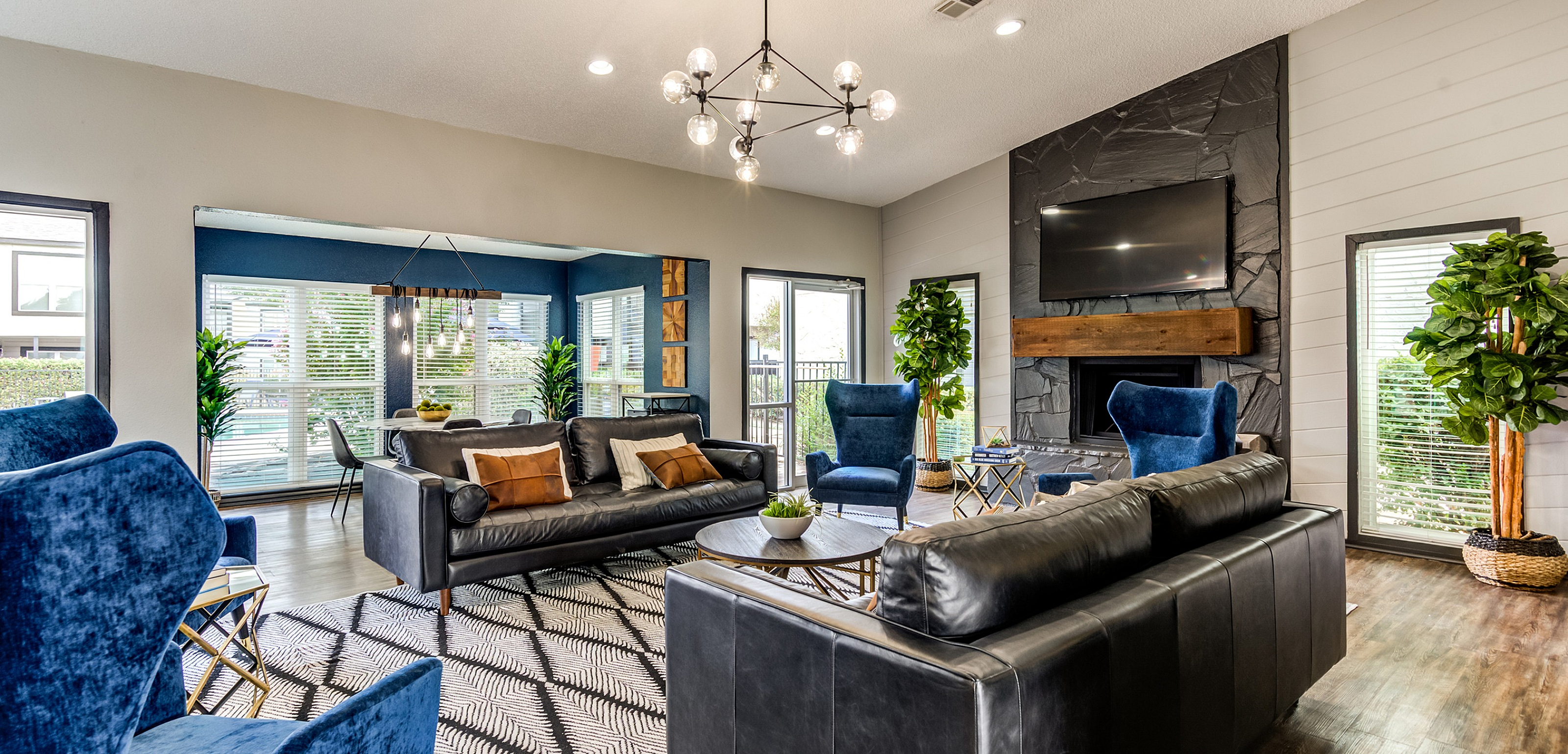 Modern living room with a chic chandelier, plush blue chairs, black leather sofas, and a stylish fireplace.