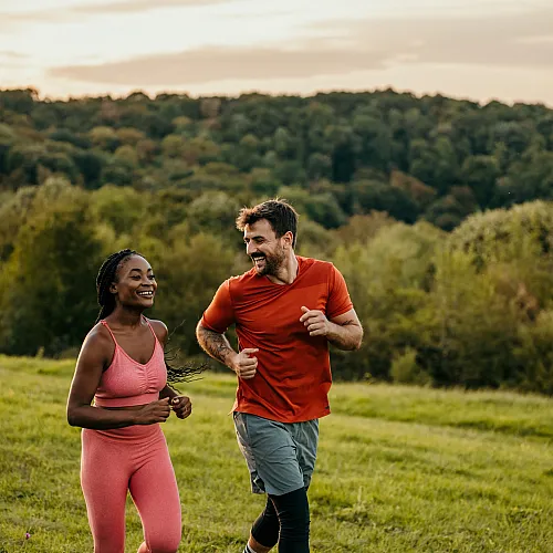 Happy couple jogging through a lush, green landscape during a picturesque sunrise.
