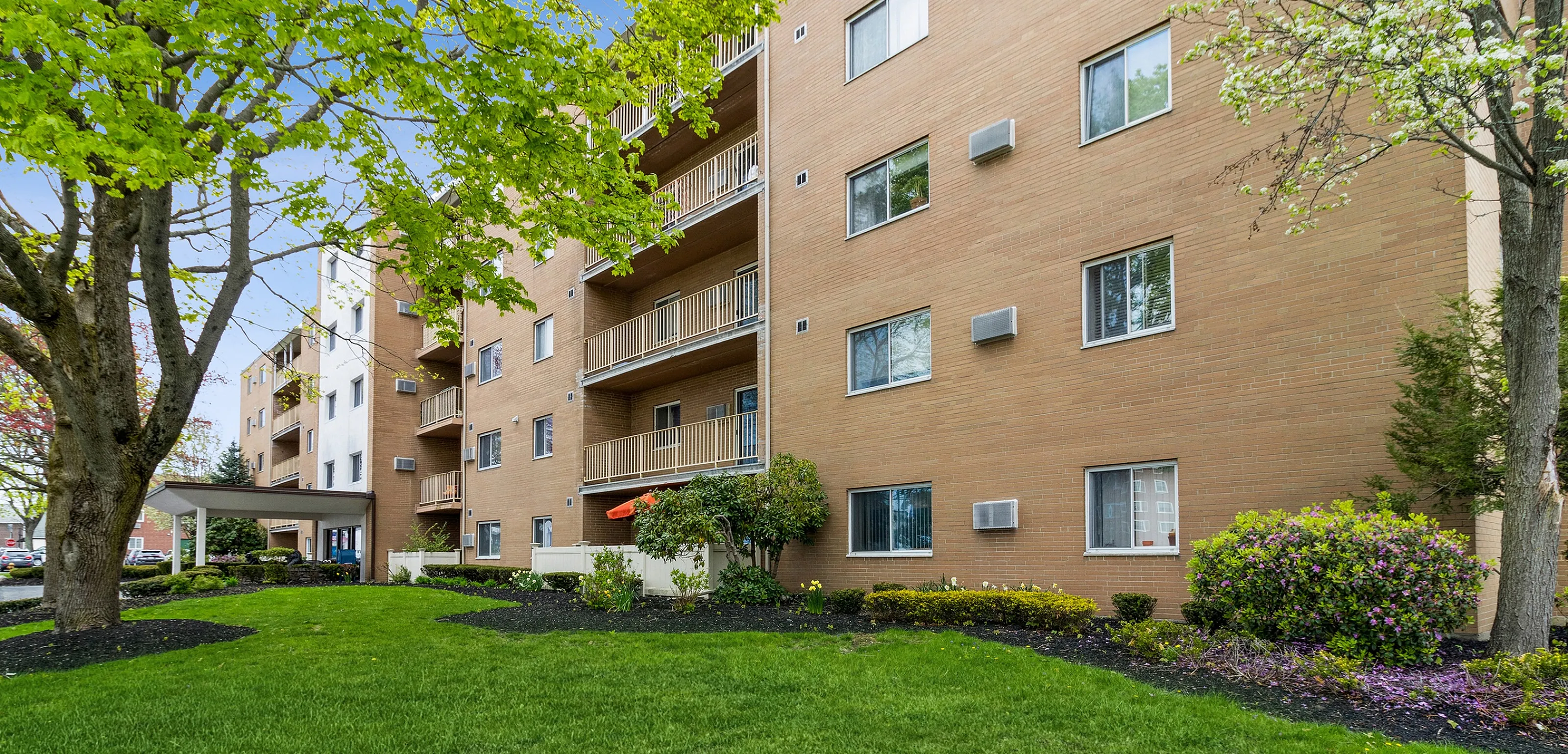Charming apartment building with a lush green lawn and vibrant landscaping, offering a serene and inviting atmosphere.