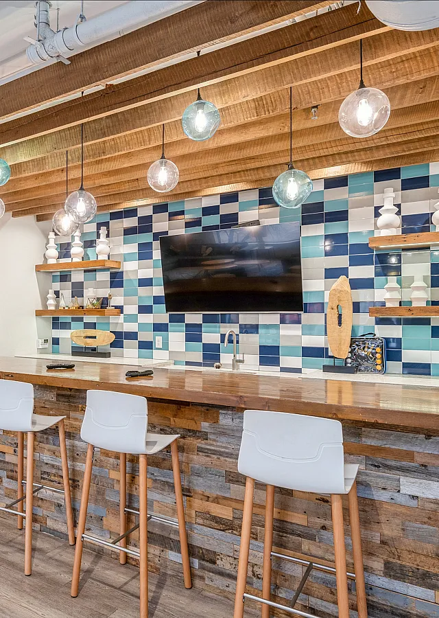 Contemporary lounge area with a stylish wooden bar, modern pendant lighting, and vibrant blue tile accents.