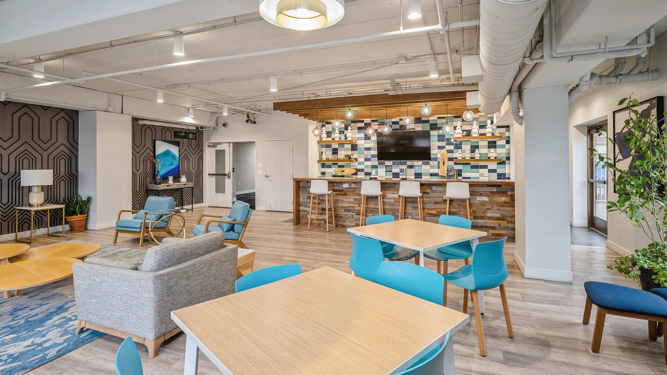 Modern co-working space with vibrant decor, featuring cozy seating areas, a sleek bar with stylish stools, and colorful geometric patterns.