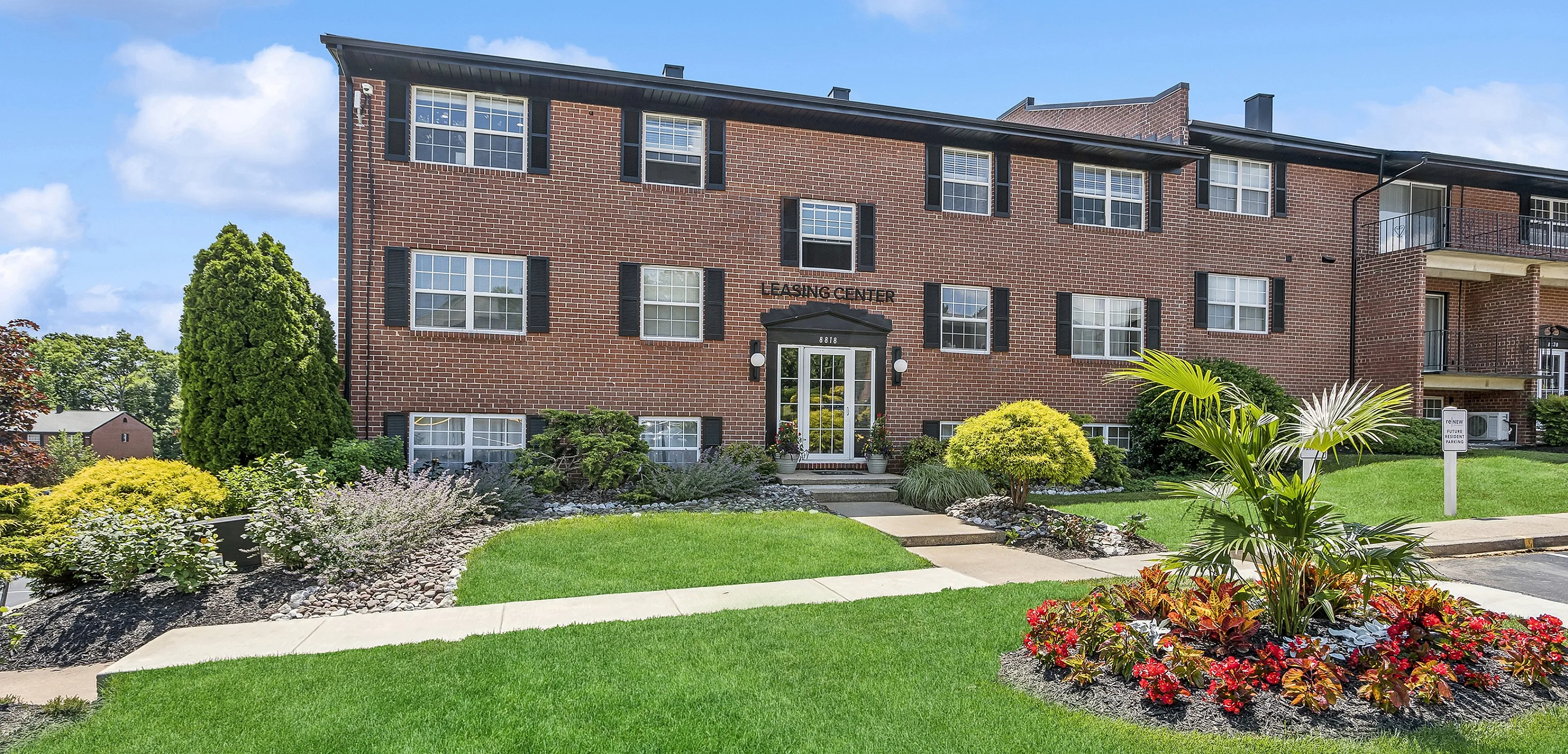 Charming brick apartment building with lush landscaping and bright green lawns, inviting entrance labeled Leasing Center.
