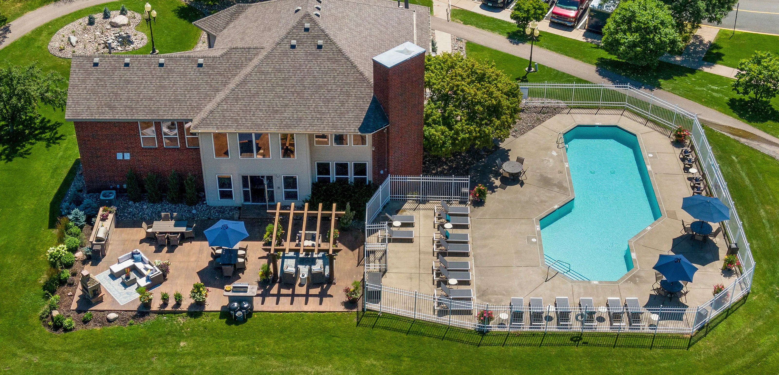 Elevated view of a luxurious apartment complex showcasing a pristine outdoor pool and sun-drenched patio with seating, surrounded by lush green lawns and vibrant landscaping.