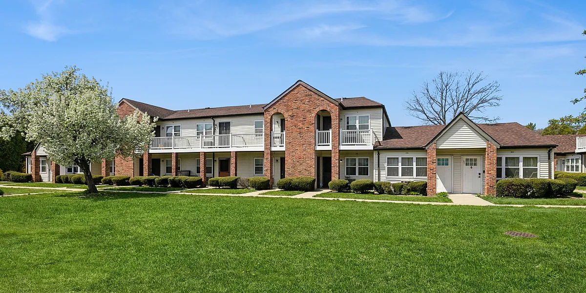 Charming brick apartment complex with lush green lawn and beautiful blue sky backdrop, offering serene and comfortable living.