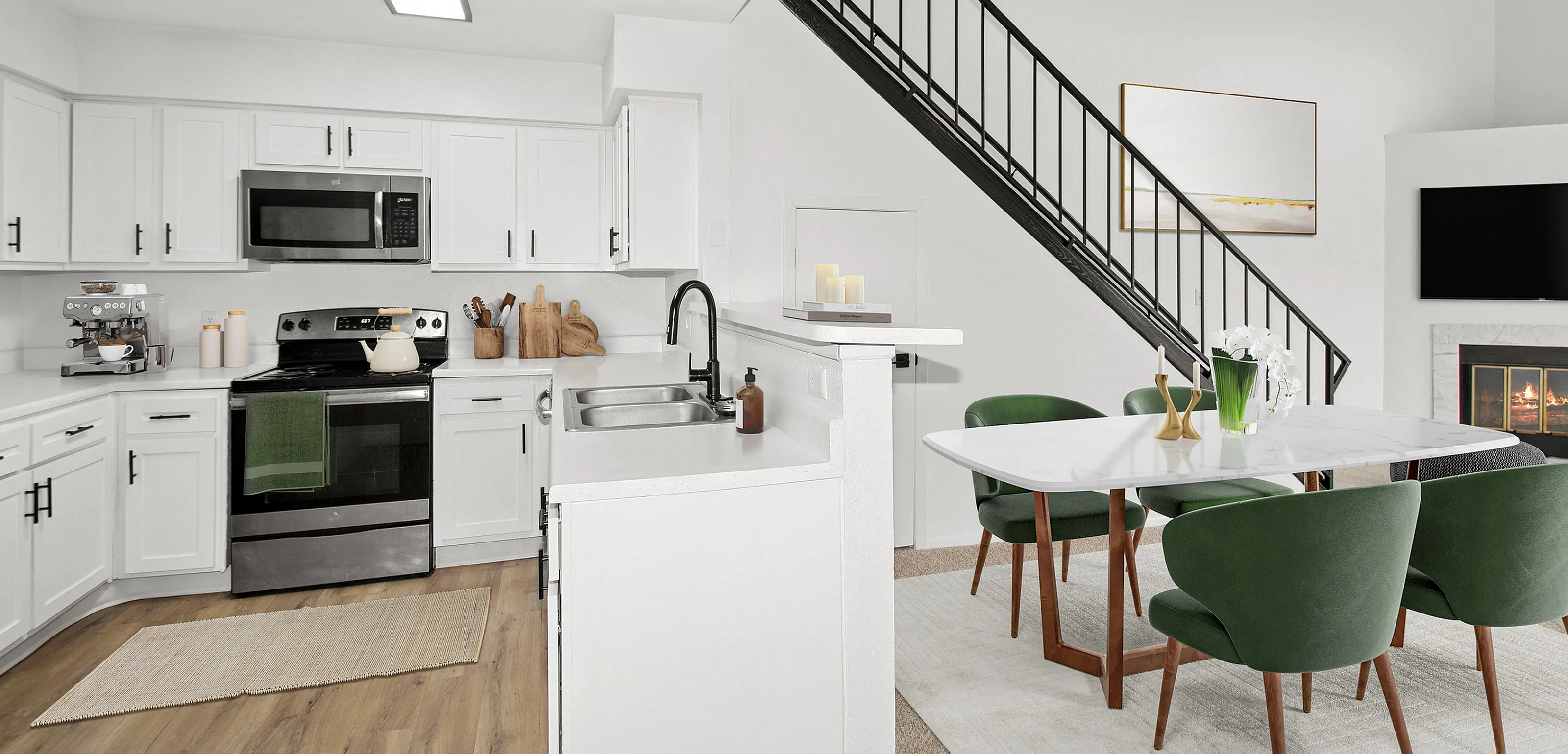 Modern open-concept kitchen and dining area with sleek white cabinetry, stainless steel appliances, chic green chairs, and a cozy fireplace.