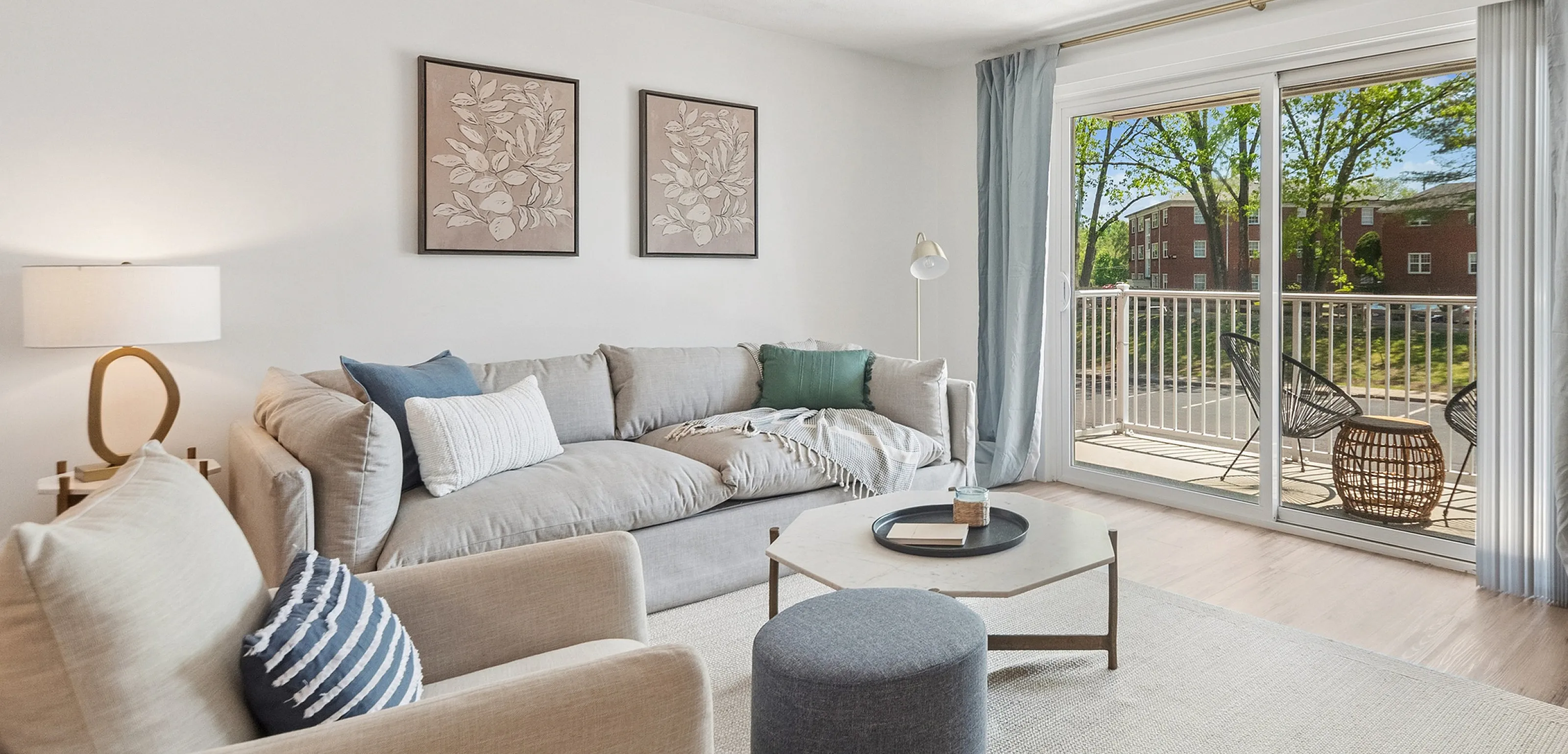 Bright and modern living room with natural light, featuring a cozy sectional sofa, chic decor, and access to a spacious balcony with green views.