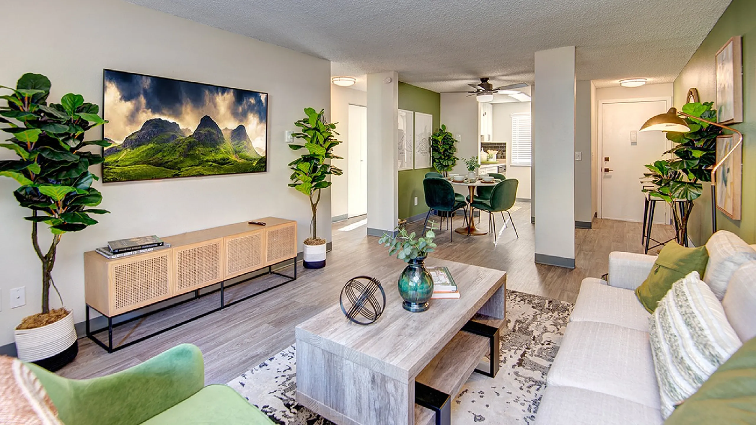 Modern and inviting living area with stylish decor, featuring a comfortable sofa, green accent chairs, wall art, and lush houseplants, leading into a chic dining space and well-lit kitchen at ReNew Dash Point.